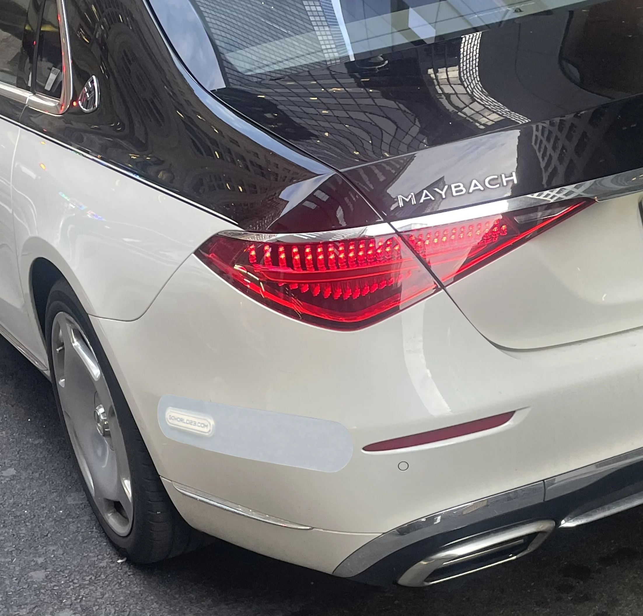 Rear view of a luxury Maybach car with a black roof and white body, parked on the street, with reflections of buildings on the car's surface.