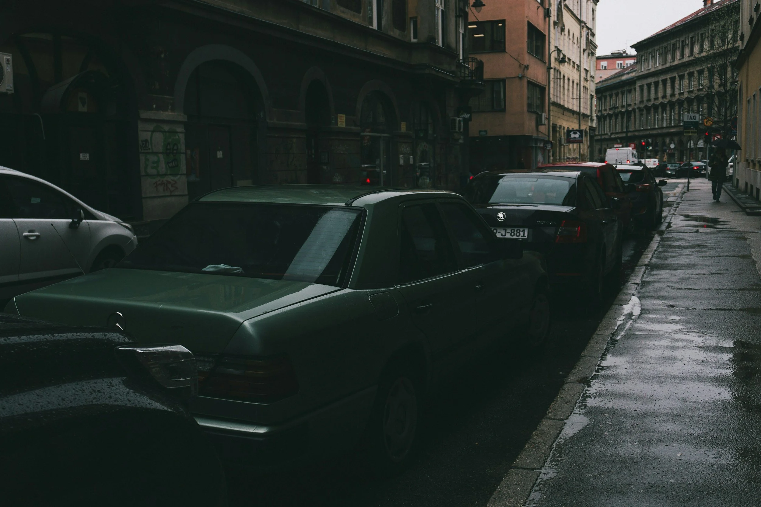 Photos of two cars parked along the sidewalk in a city. One is green the other is black.