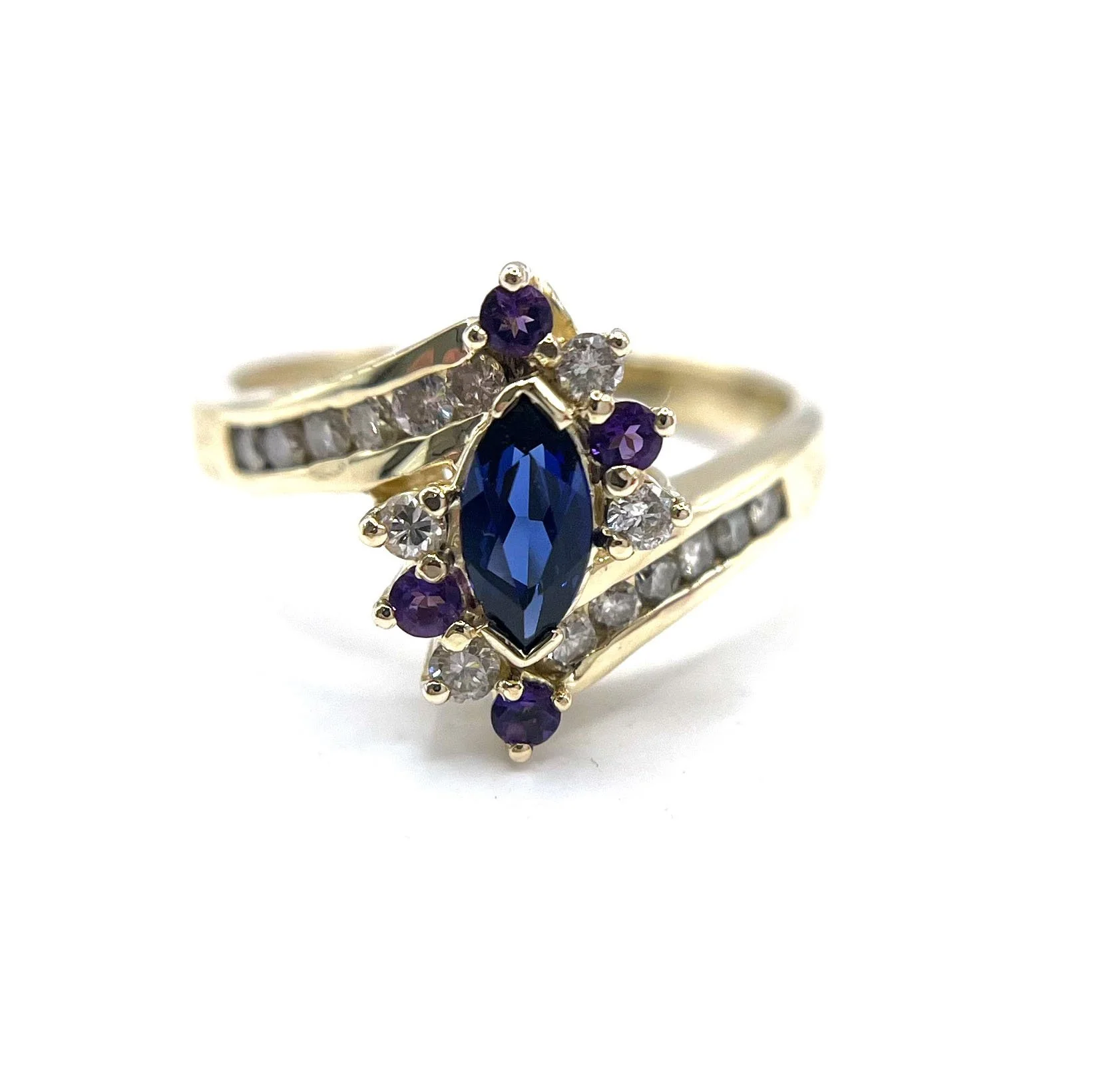 Gold ring with a central marquise-cut blue gemstone, surrounded by smaller purple and clear gemstones with additional clear gemstones set along the band.
