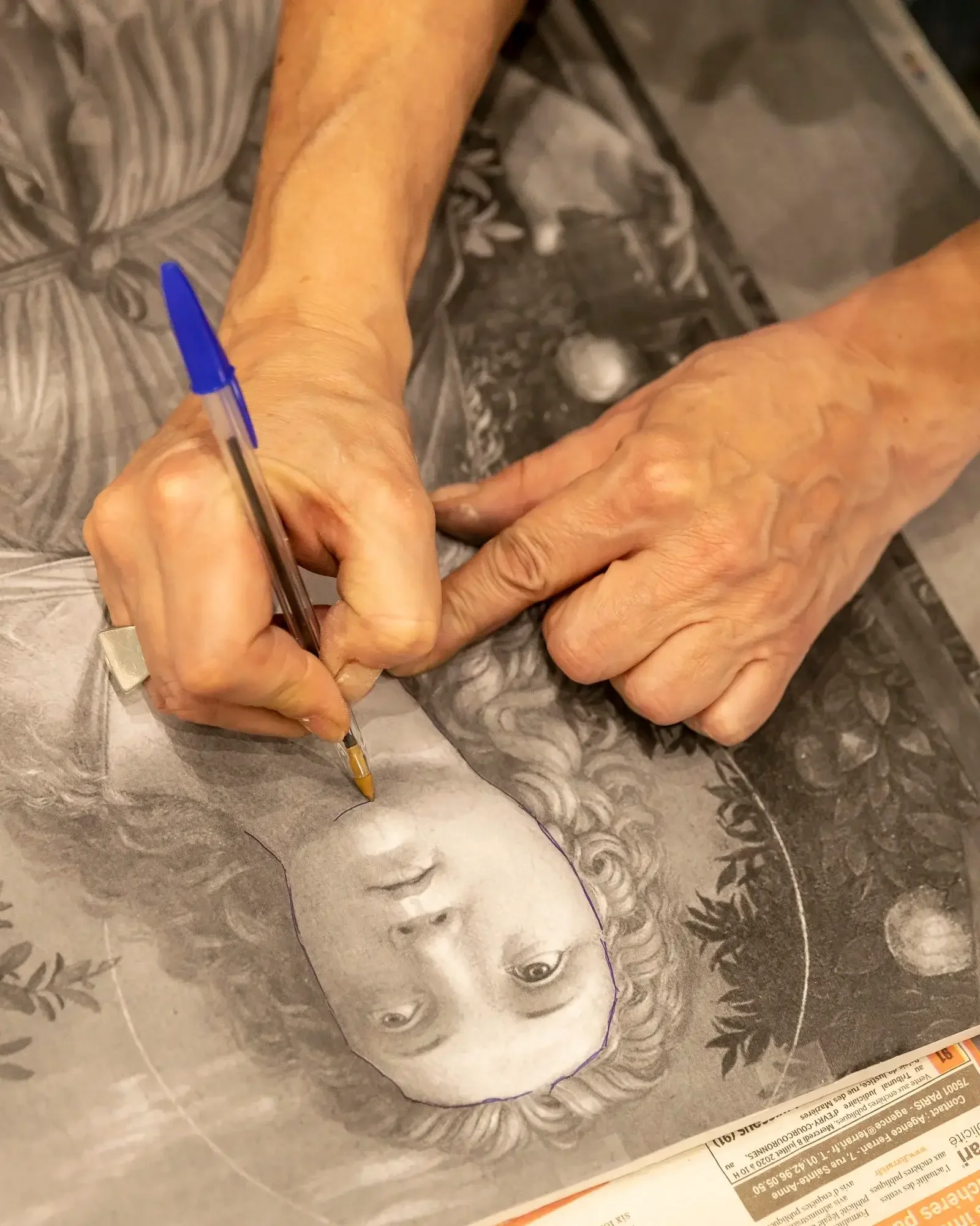 Une personne utilise un stylo pour délimiter un portrait en noir et blanc d'une femme avec des cheveux bouclés, entourée d'illustrations de plantes et de planètes.