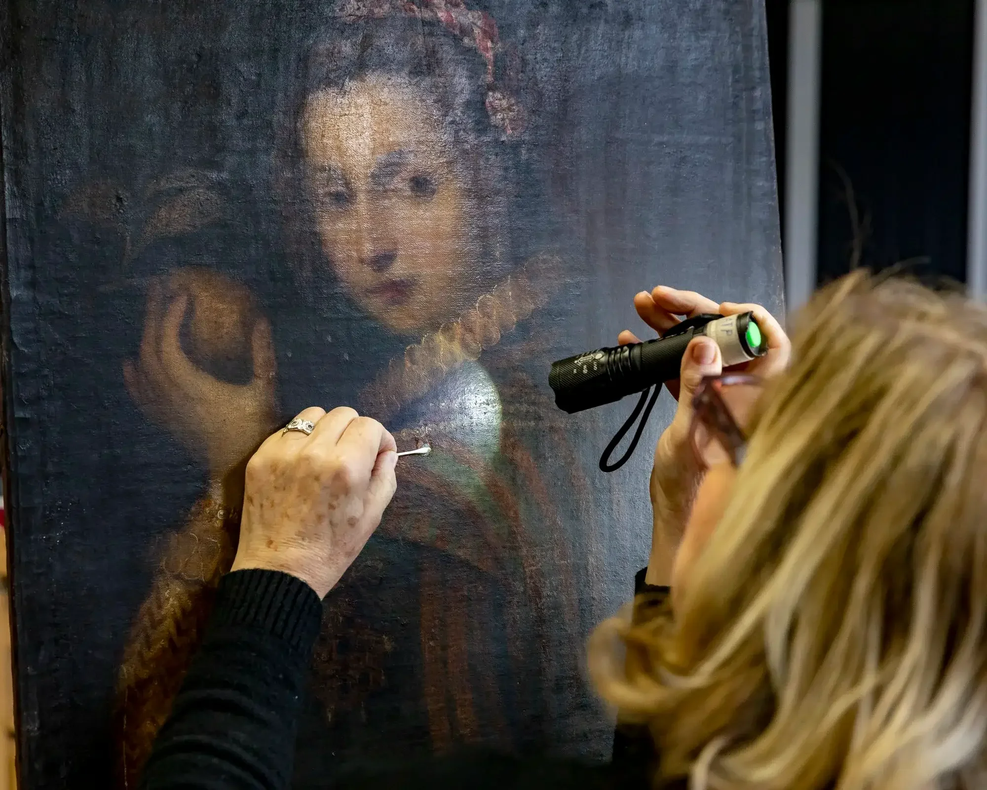 Une personne restaure une peinture classique représentant une femme avec un collier de perles.