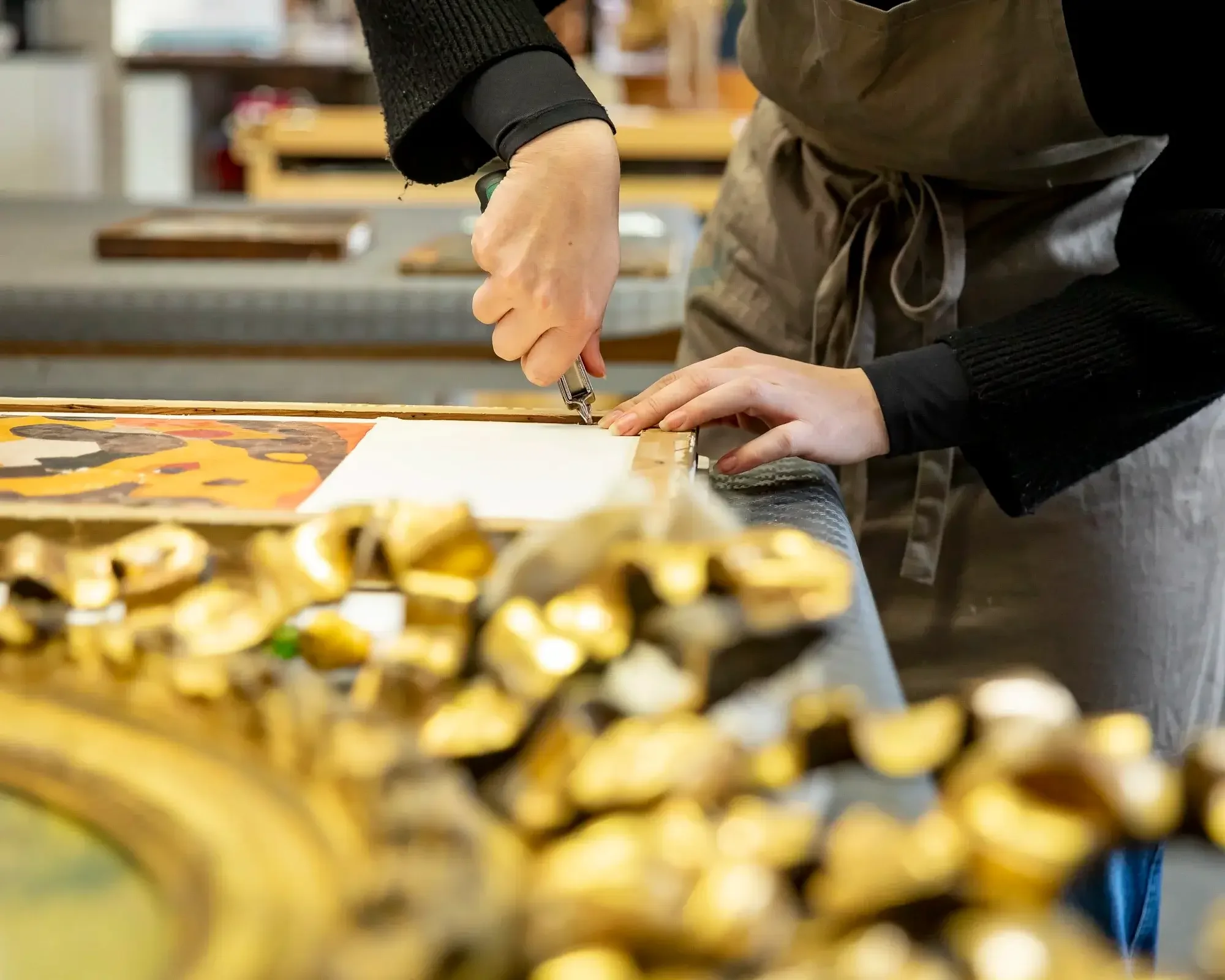 Une personne utilisant un stylo pour marquer une toile dans un atelier d'art, avec des objets dorés en premier plan.
