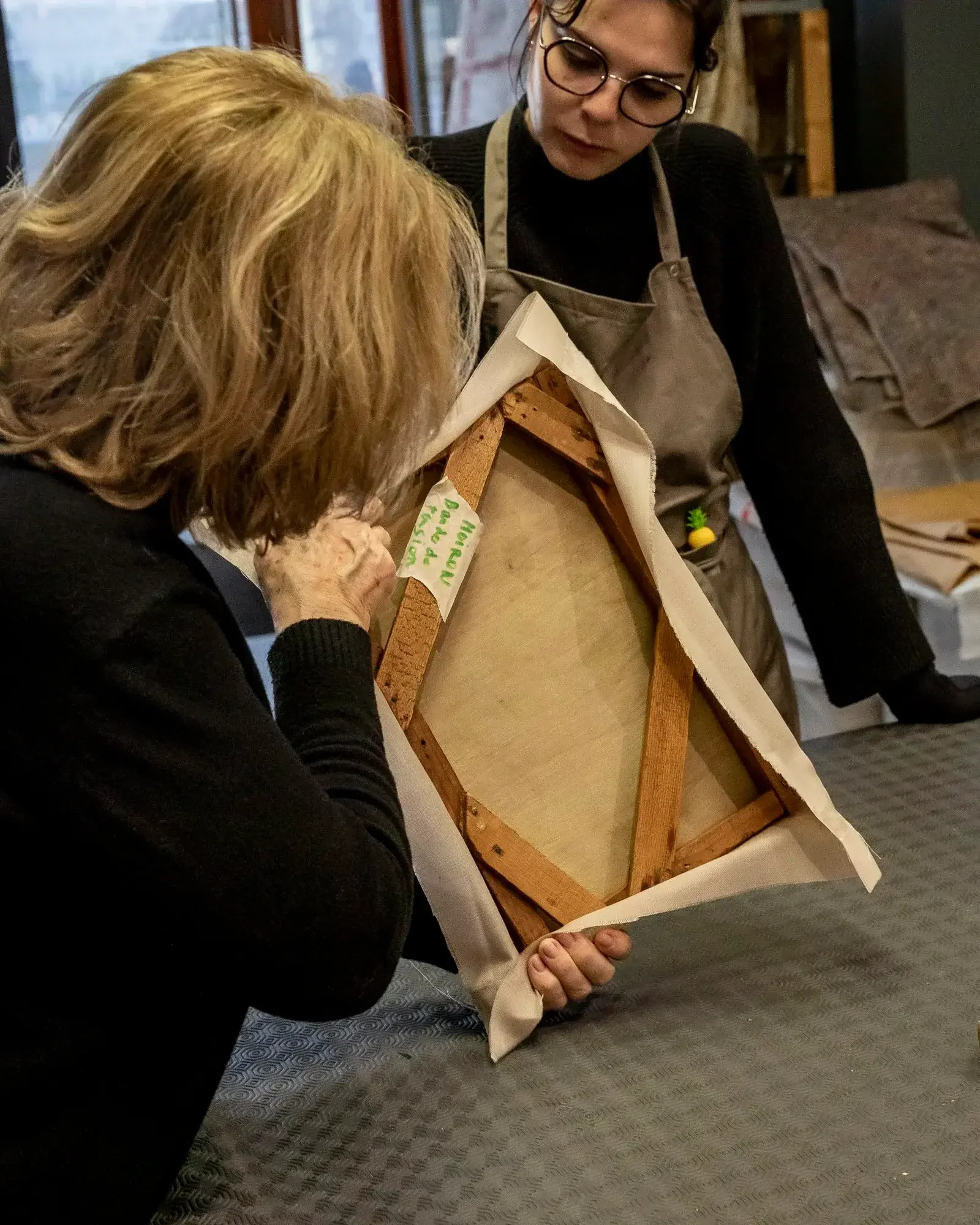 Deux femmes examinent un cadre en bois protégé par du papier d'emballage dans une pièce intérieure