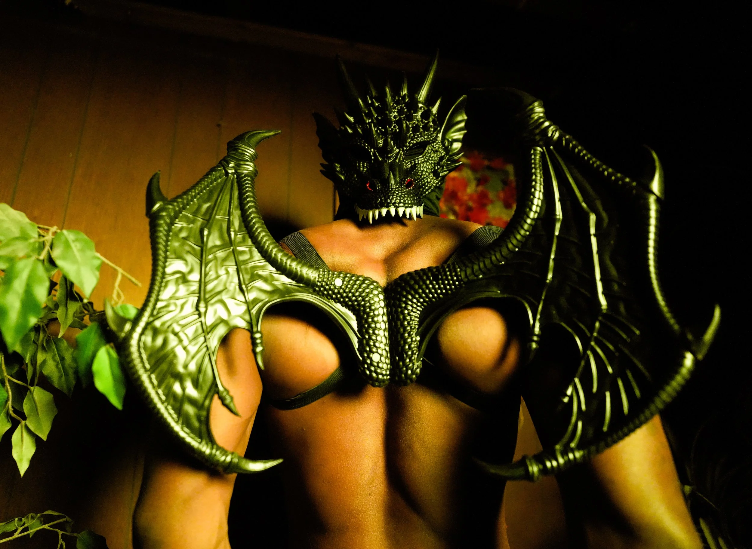Person wearing a detailed black and green dragon or demon mask and large leather wings cosplay costume.