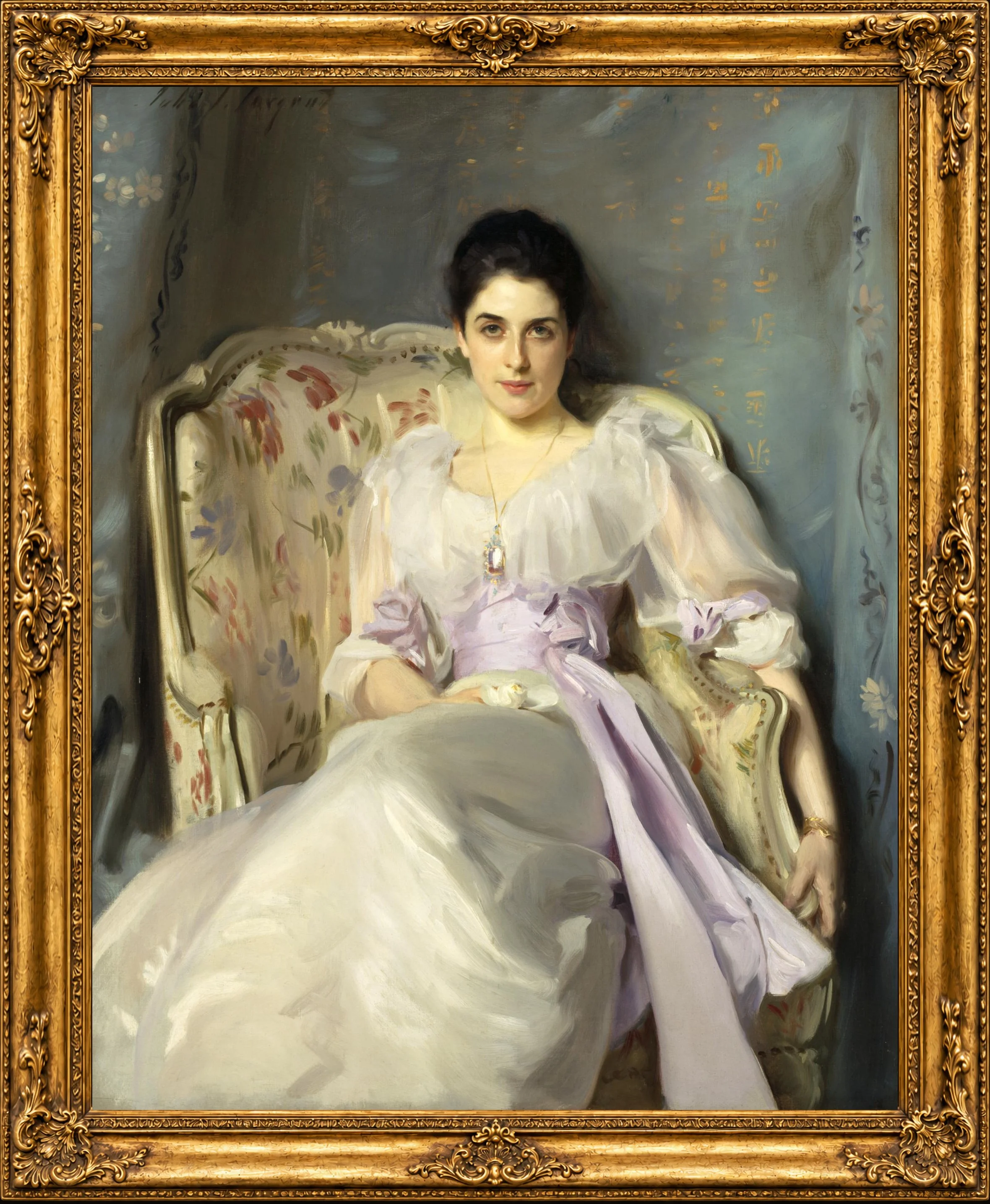 A classical portrait painting of a woman with dark hair, wearing a white dress, sitting on an ornate chair with a floral cushion, framed with an elaborate gold frame.