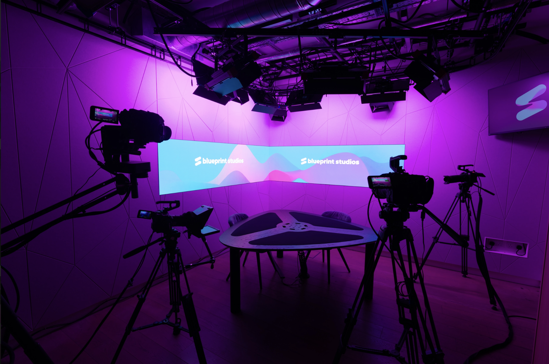 Studio with 4 cameras, table chairs and LED screen background showing blueprint studios branding