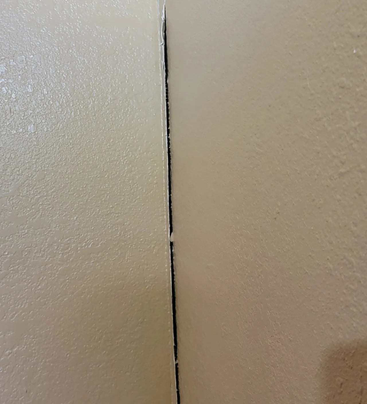 Close-up of a gap between two painted wall surfaces, with some visible debris in the gap.