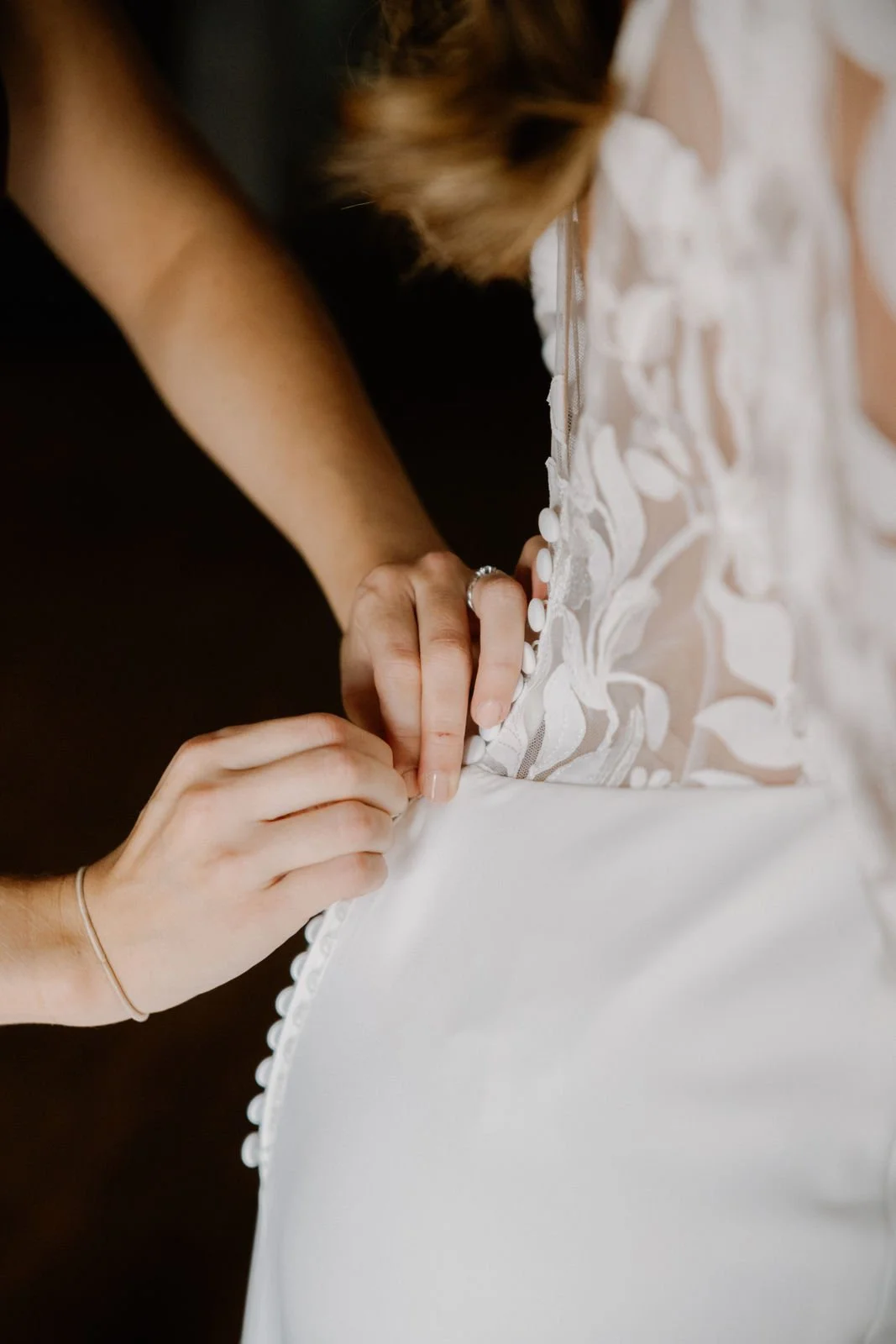 Nahaufnahme einer Braut, wo die Hochzeitsplanerin assistiert die Knöpfe des Hochzeitskleids zu schließen