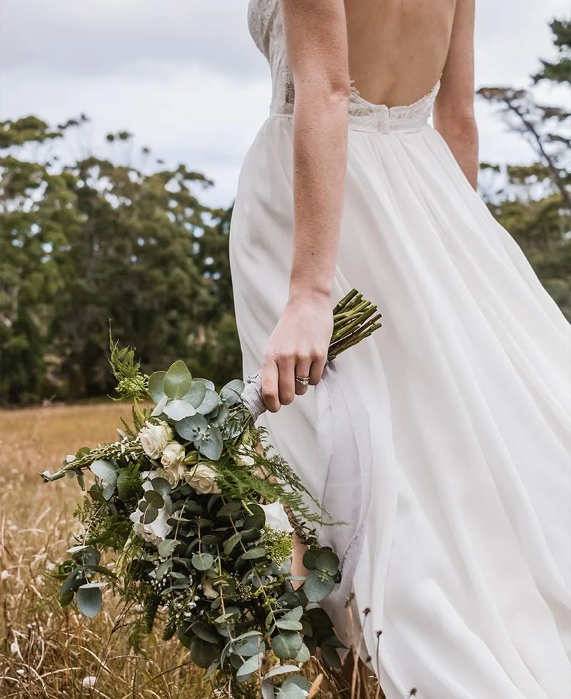 Braut in fließendem Hochzeitskleid hält einen großen Brautstrauß mit Eukalyptus und weißen Blüten – freie Trauung in der Schweiz im Grünen.