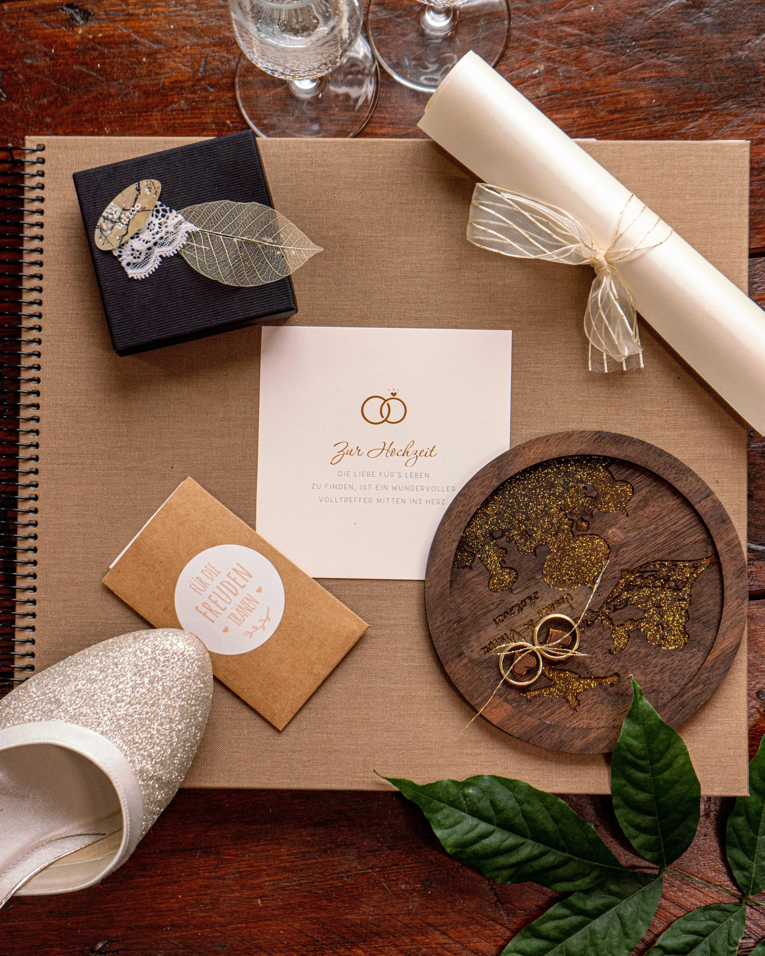 Hochzeitsdeko mit Einladung, Geschenk, Kerze, Weltkarte und Blättern auf Holz.