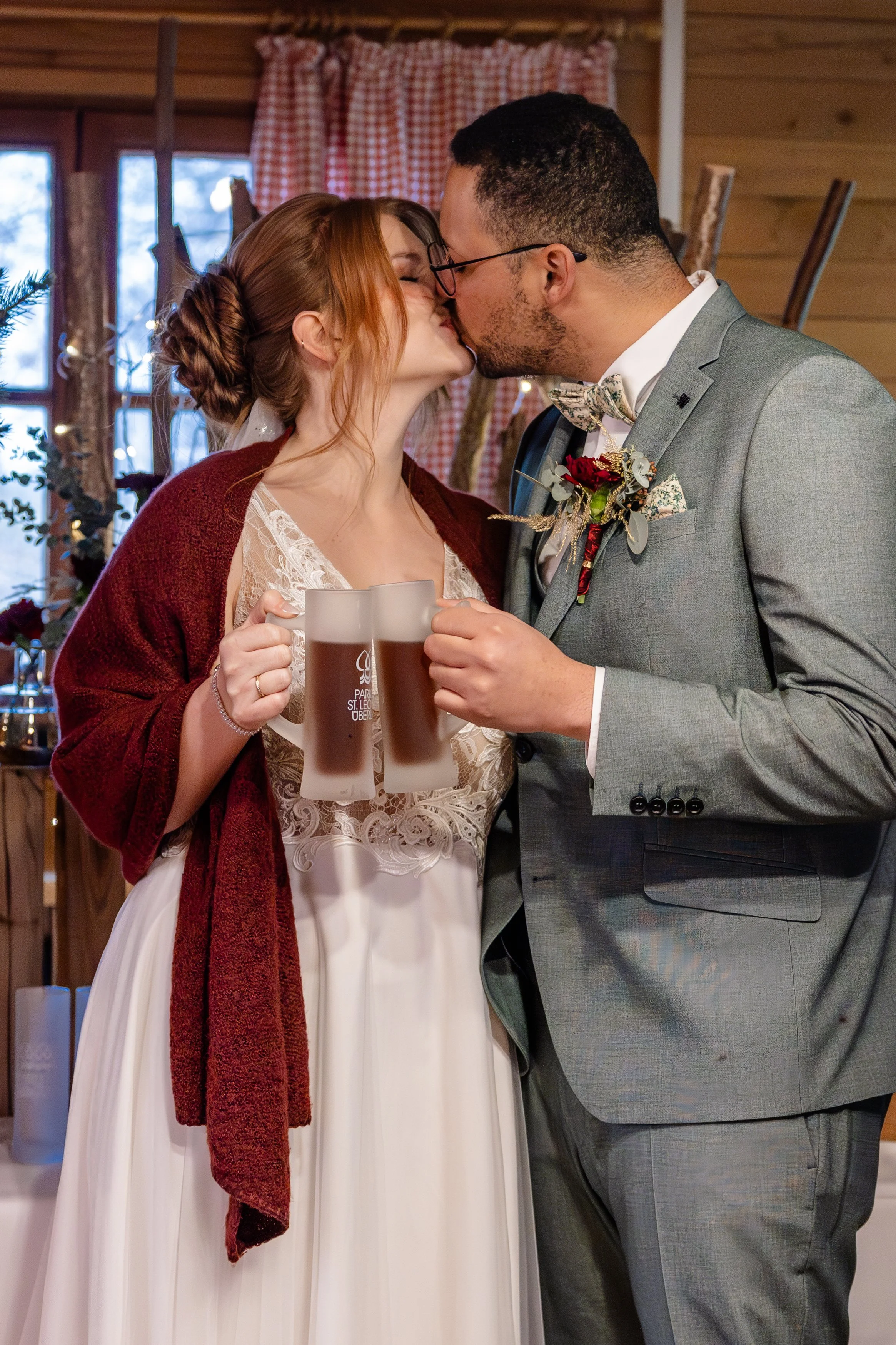 Hochzeitspaar küsst sich bei Feierlichkeiten und einem Glühwein in der Hand