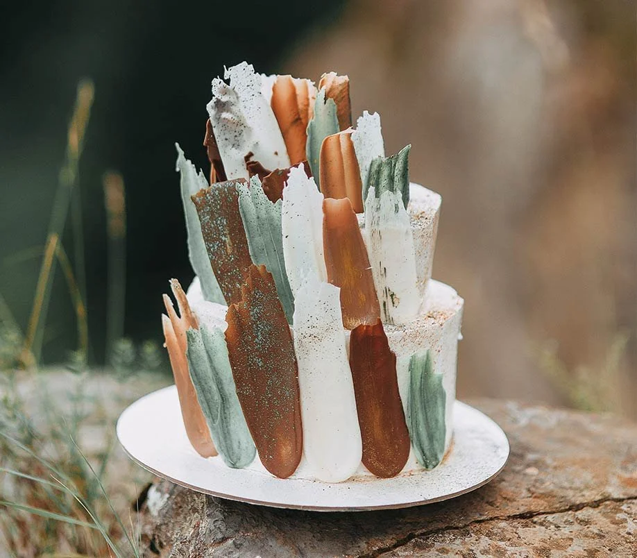 Kunstvolle Hochzeitstorte mit bunter Deko auf Baumstammteller – kreative Dessertidee für Hochzeit in der Schweiz.