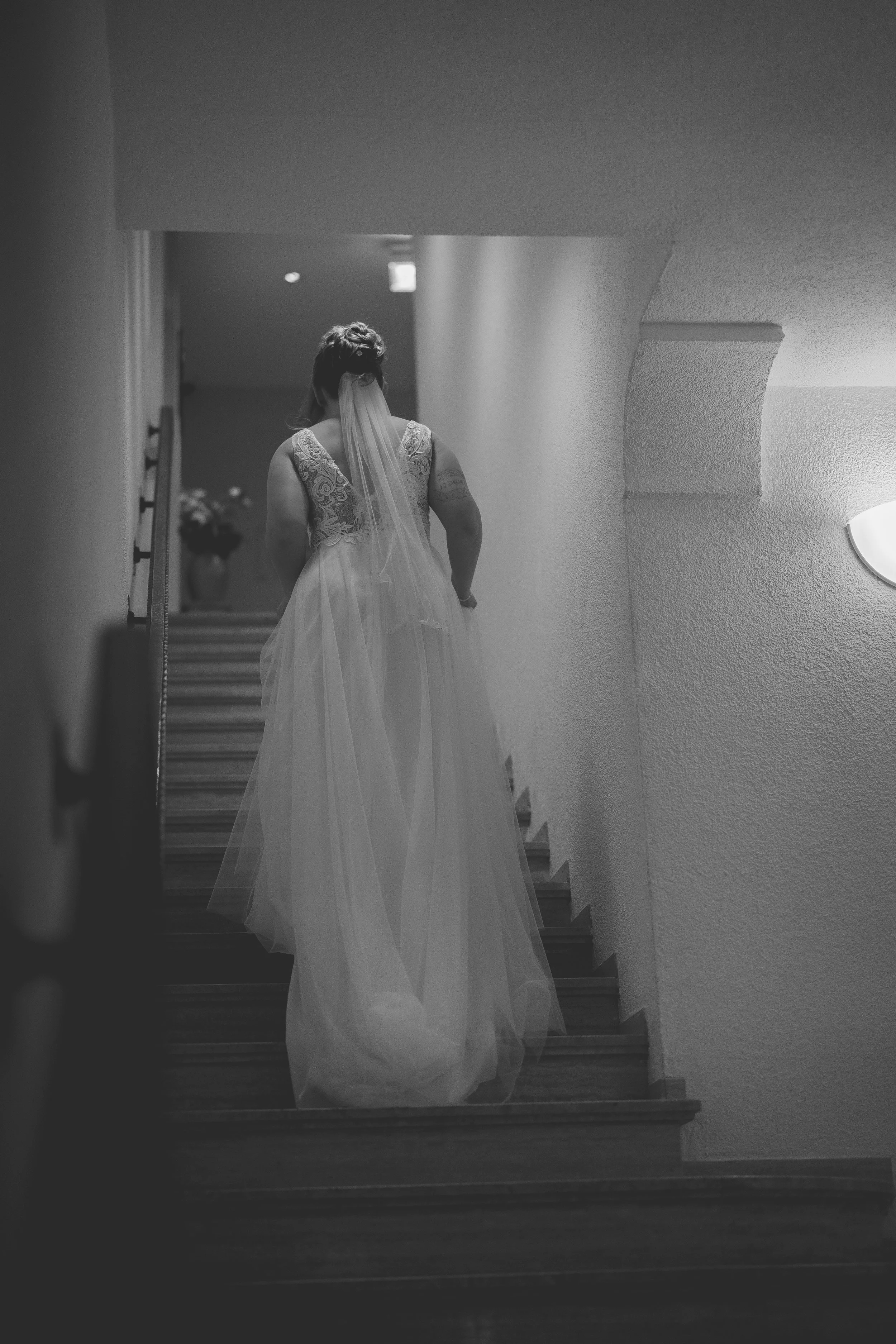 Braut in Hochzeitskleid auf Treppe, schwarz-weiß Foto.