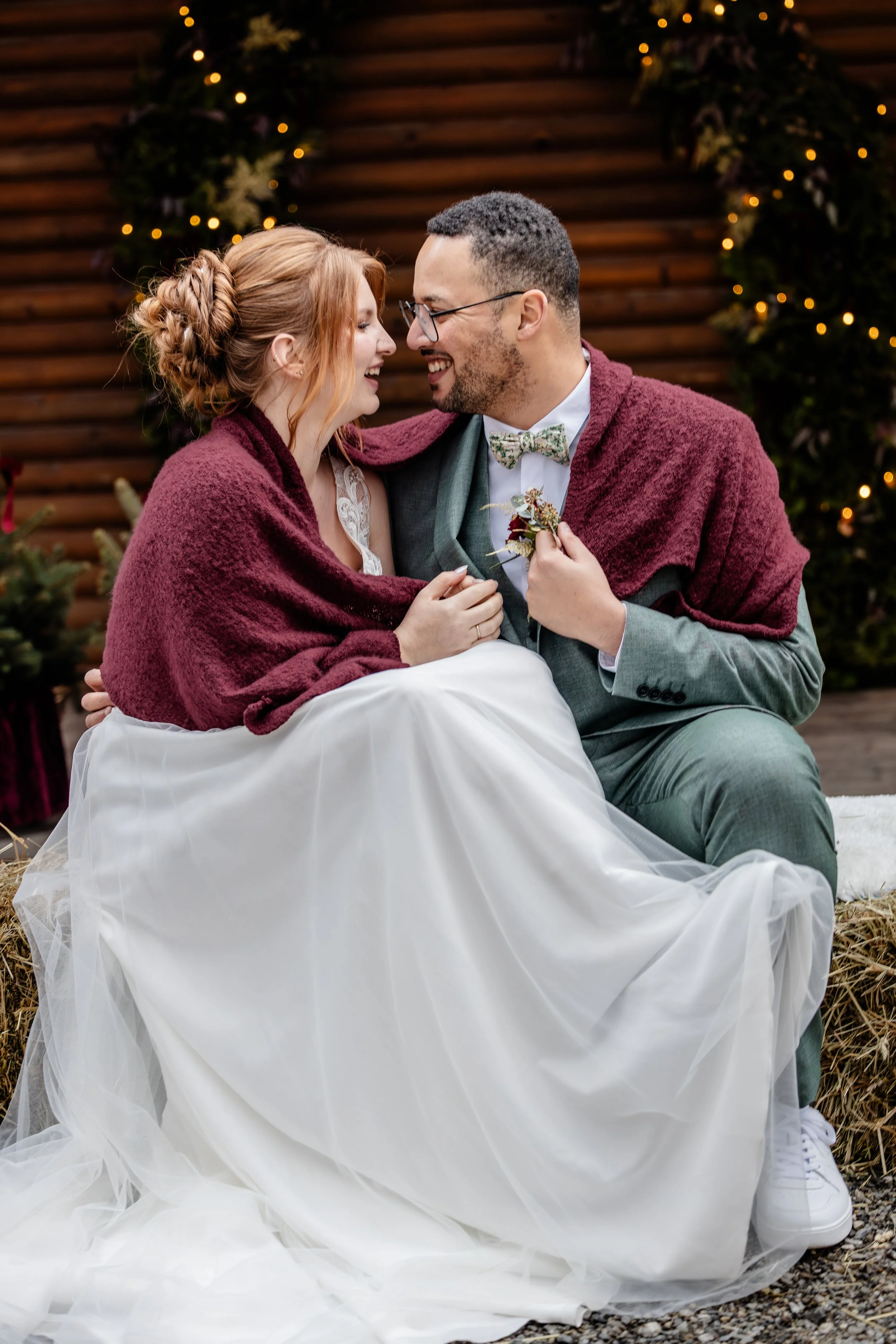 Ein frisch verheiratetes Hochzeitspaar, umgeben von Weihnachtsdekoration, sitzt liebevoll beieinander bei ihrer Winterhochzeit.