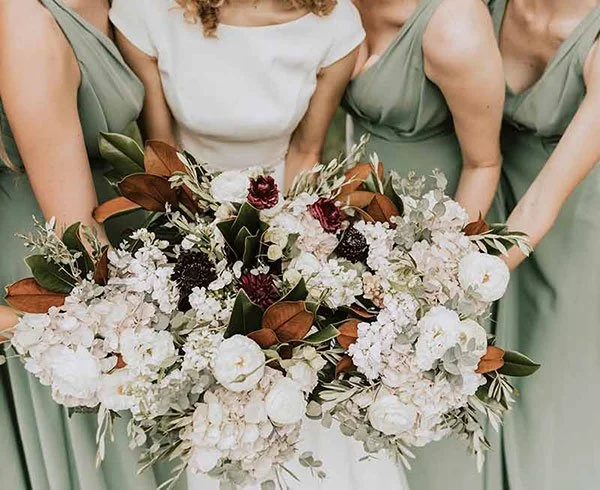 Braut mit Brautjungfern in grünen Kleidern, jede hält ein natürliches Blumenbouquet – stilvolle Hochzeitsgesellschaft im Boho-Look in der Bodenseeregion.