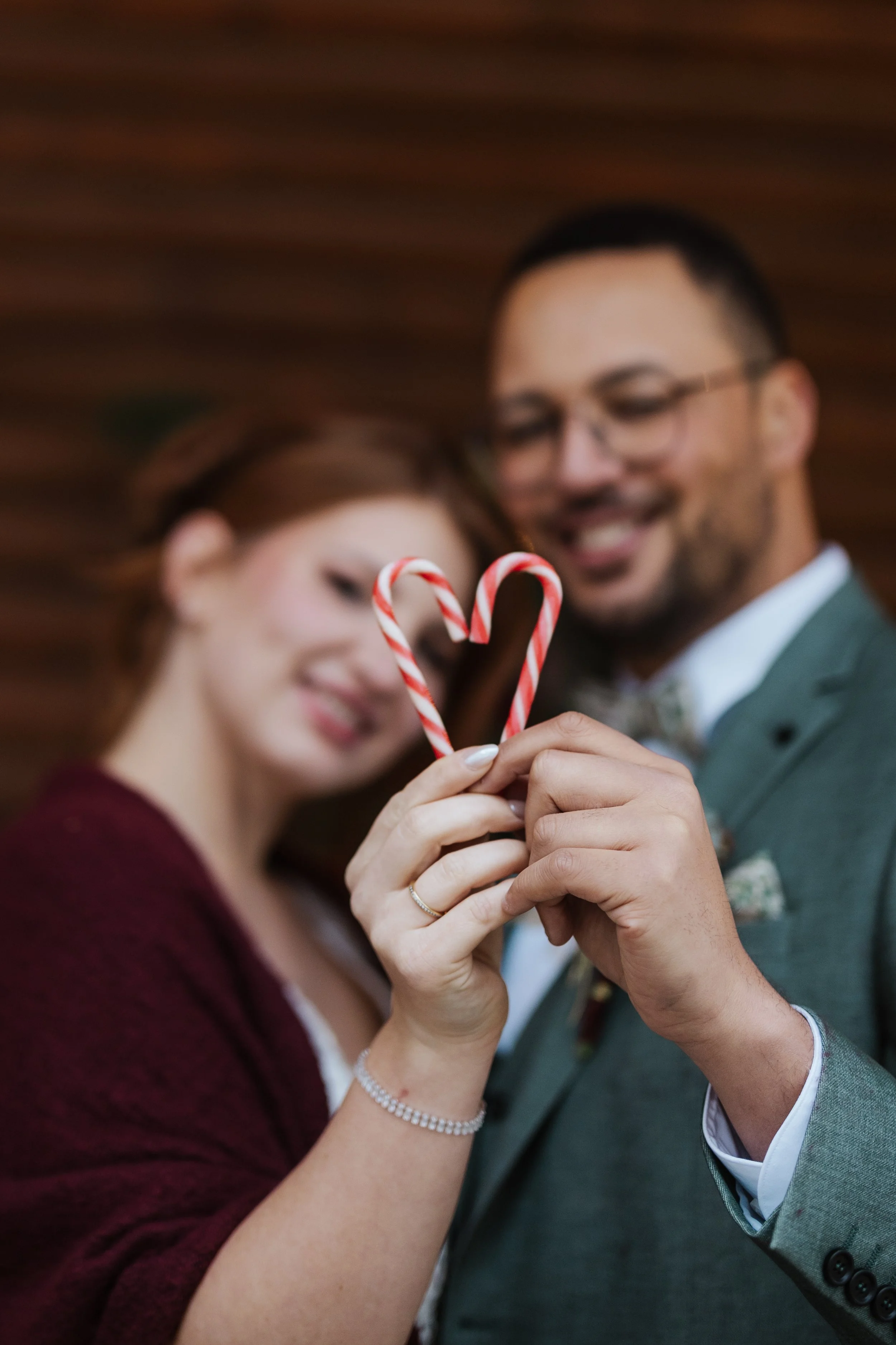 Ein Brautpaar beim Paarshooting hält Zuckerstangen, die wie ein Herz geformt sind, vor ihrem Gesicht.
