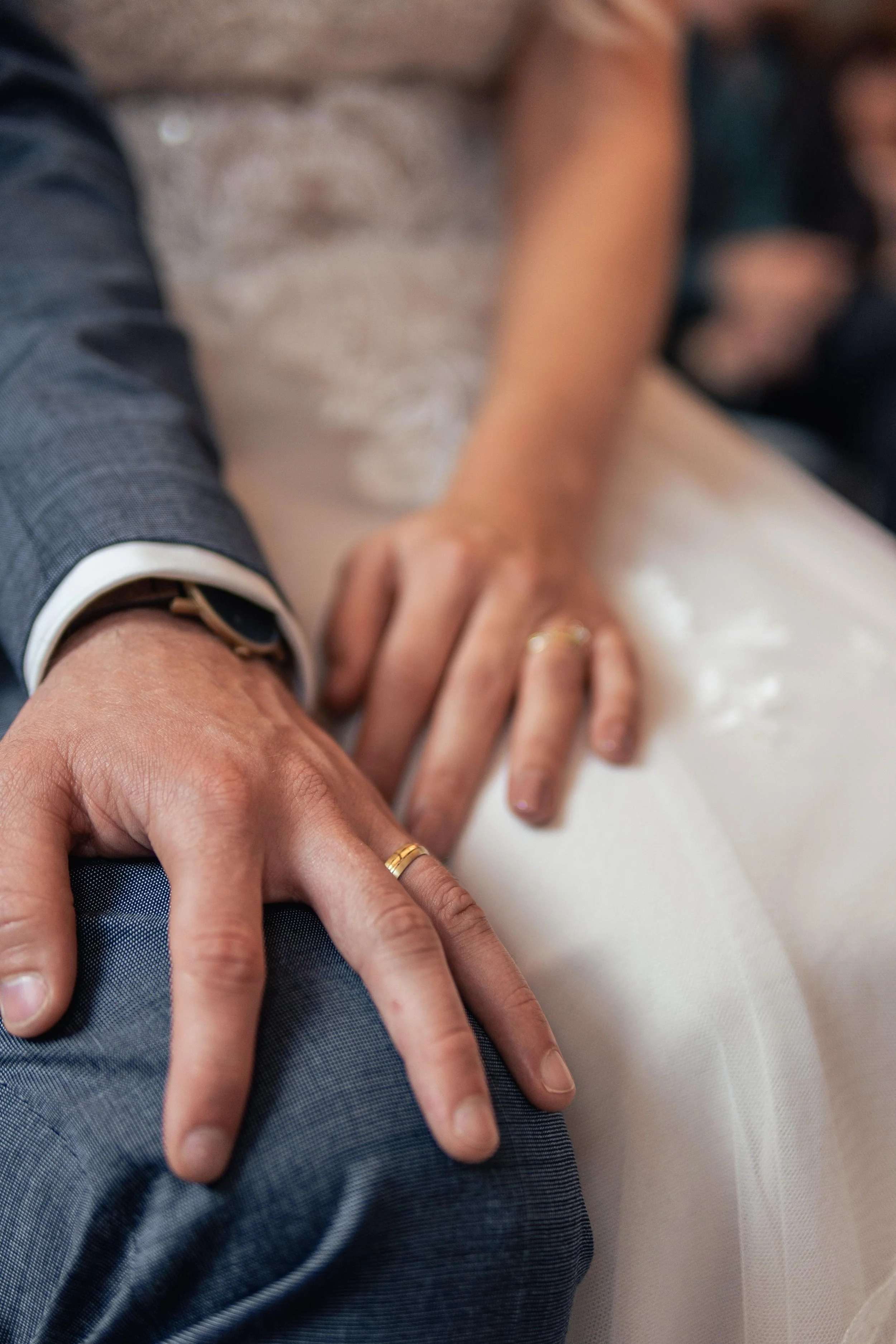 Nahaufnahme der Hände eines Paares mit Eheringen, die auf der Hochzeit auf einem weißen Kleid liegen.