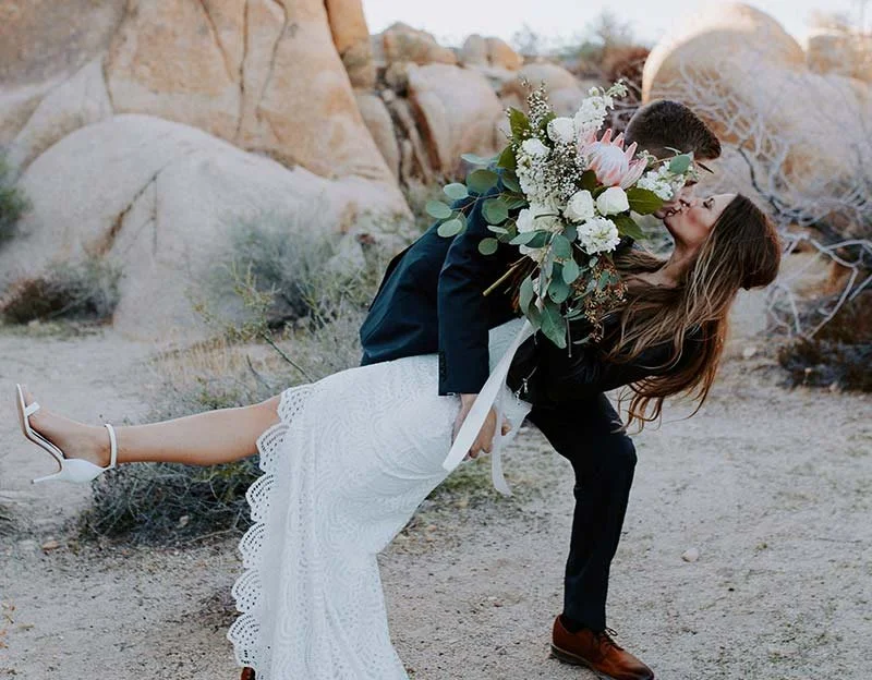 Emotionaler Hochzeitsmoment in der Natur – Braut im weißen Kleid wird vom Bräutigam vor einer Felslandschaft liebevoll gehalten und geküsst.