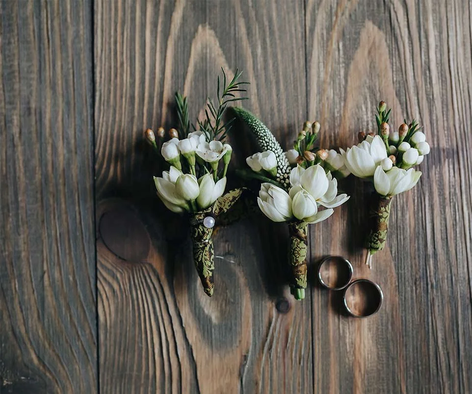 Brautaccessoires mit weißen Blüten und Eheringen auf Holztisch – liebevolle, rustikale Details für eure Hochzeit in der Schweiz.