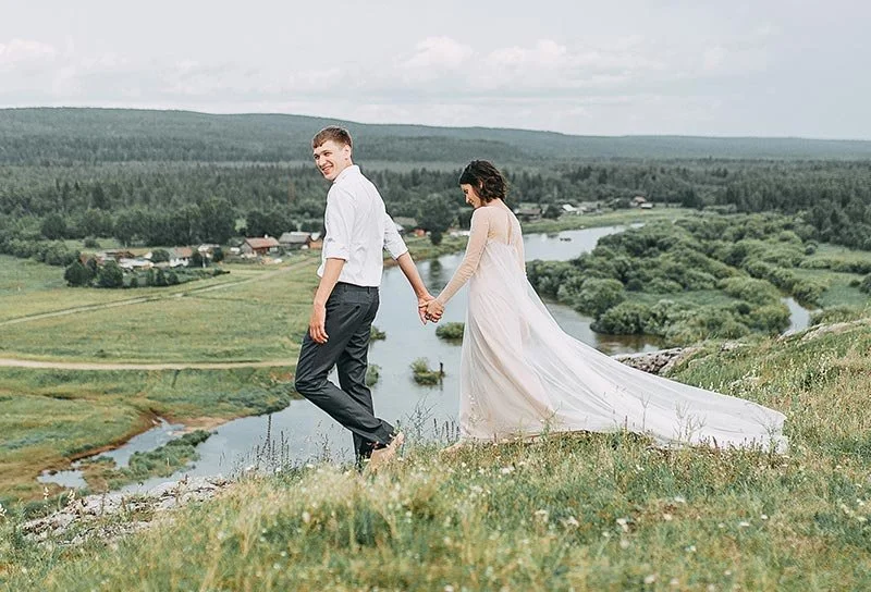 Hochzeitspaar hält Händchen auf einer grünen Wiese mit Flussblick – natürliche Hochzeitsmomente im Freien im Raum Bodensee oder St. Gallen.