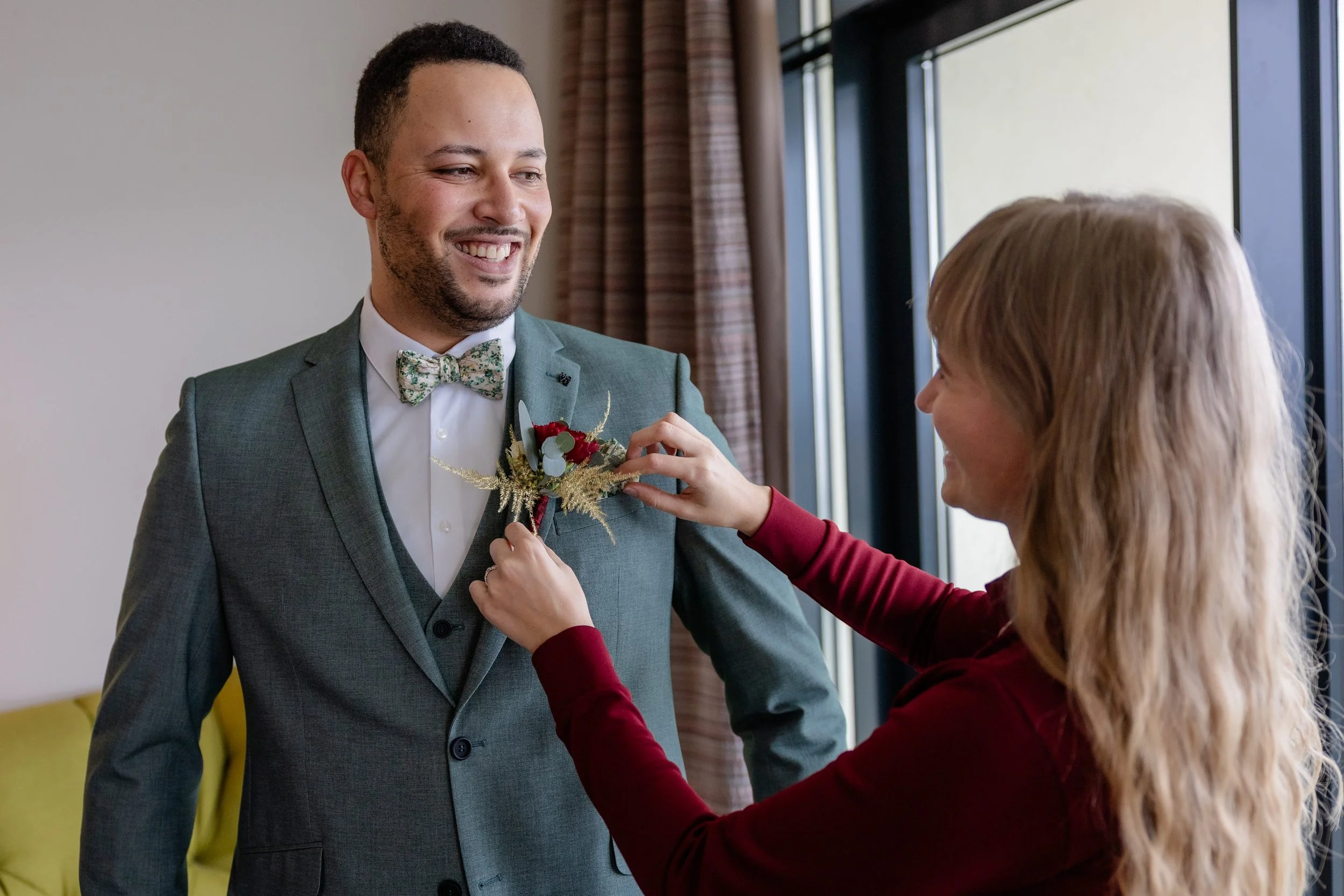 Hochzeitsplanerin unterstützt bei der Vorbereit des Bräutigams am Hochzeitstag, indem sie das Boutonnière am Hochzeitsanzug befestigt.