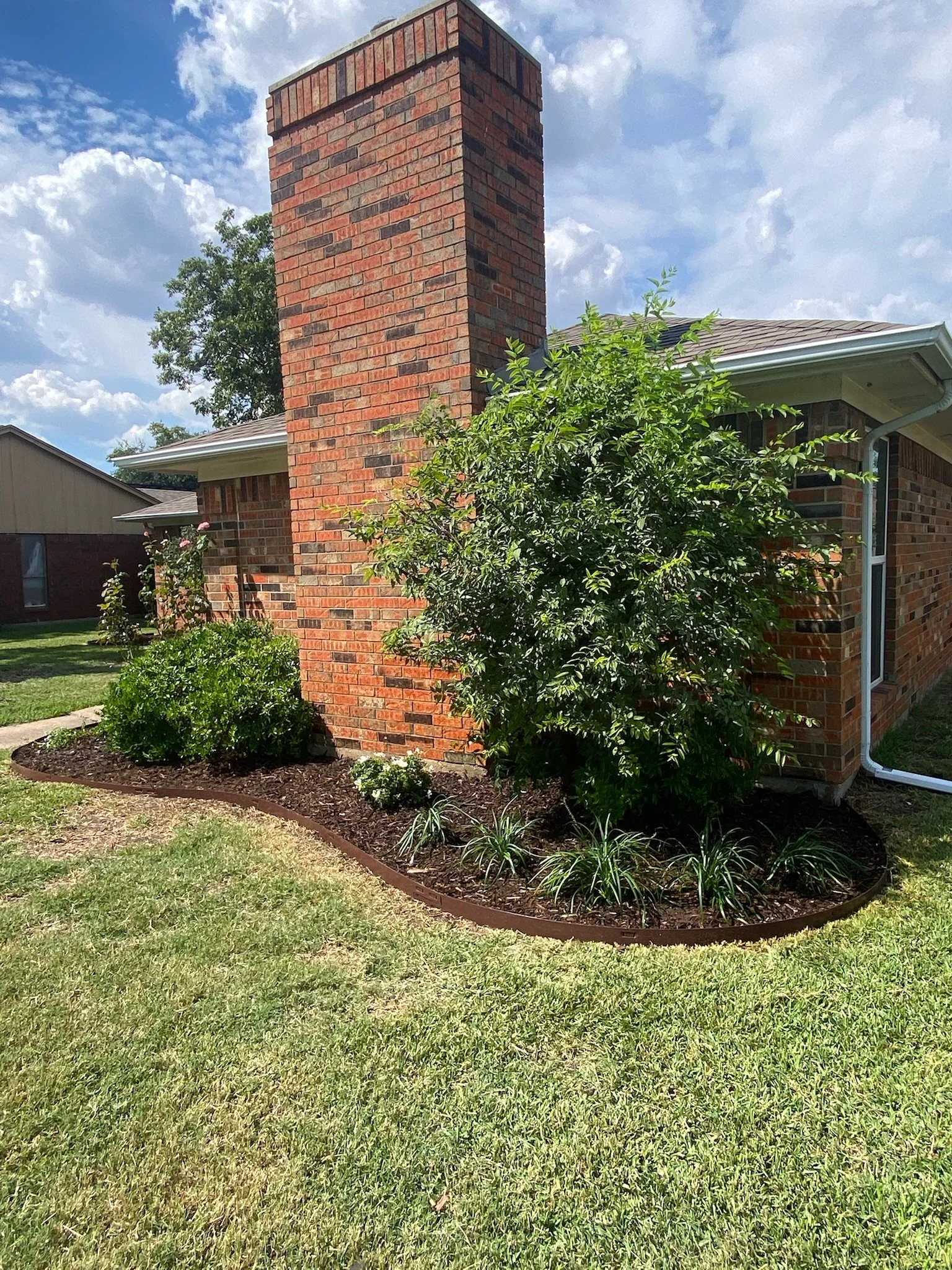 After photo of a redesigned garden bed featuring clean edging, native plants, and fresh mulch in Garland, TX.