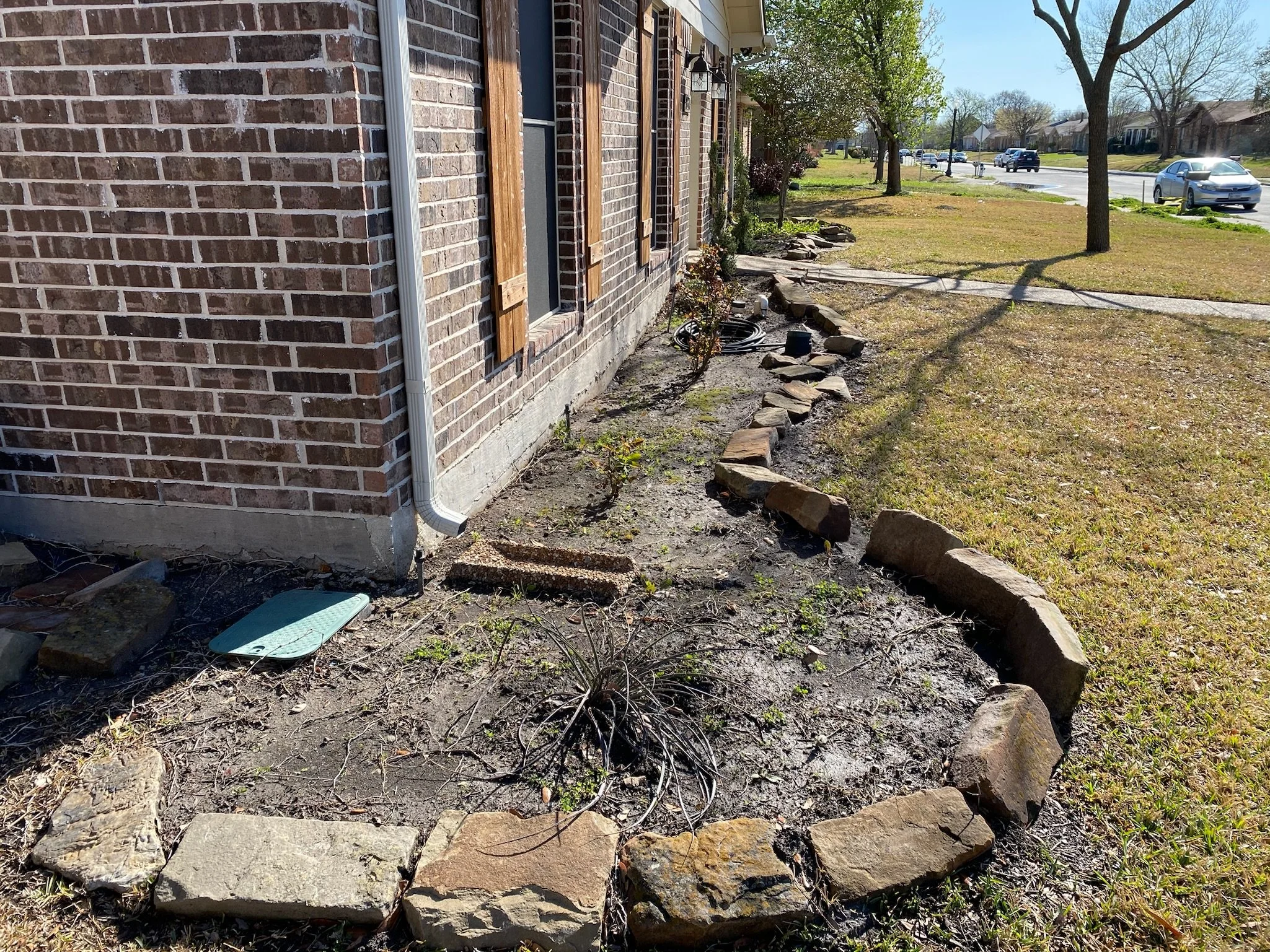 Before photo of garden bed in Garland, TX with uneven edges and no mulch.