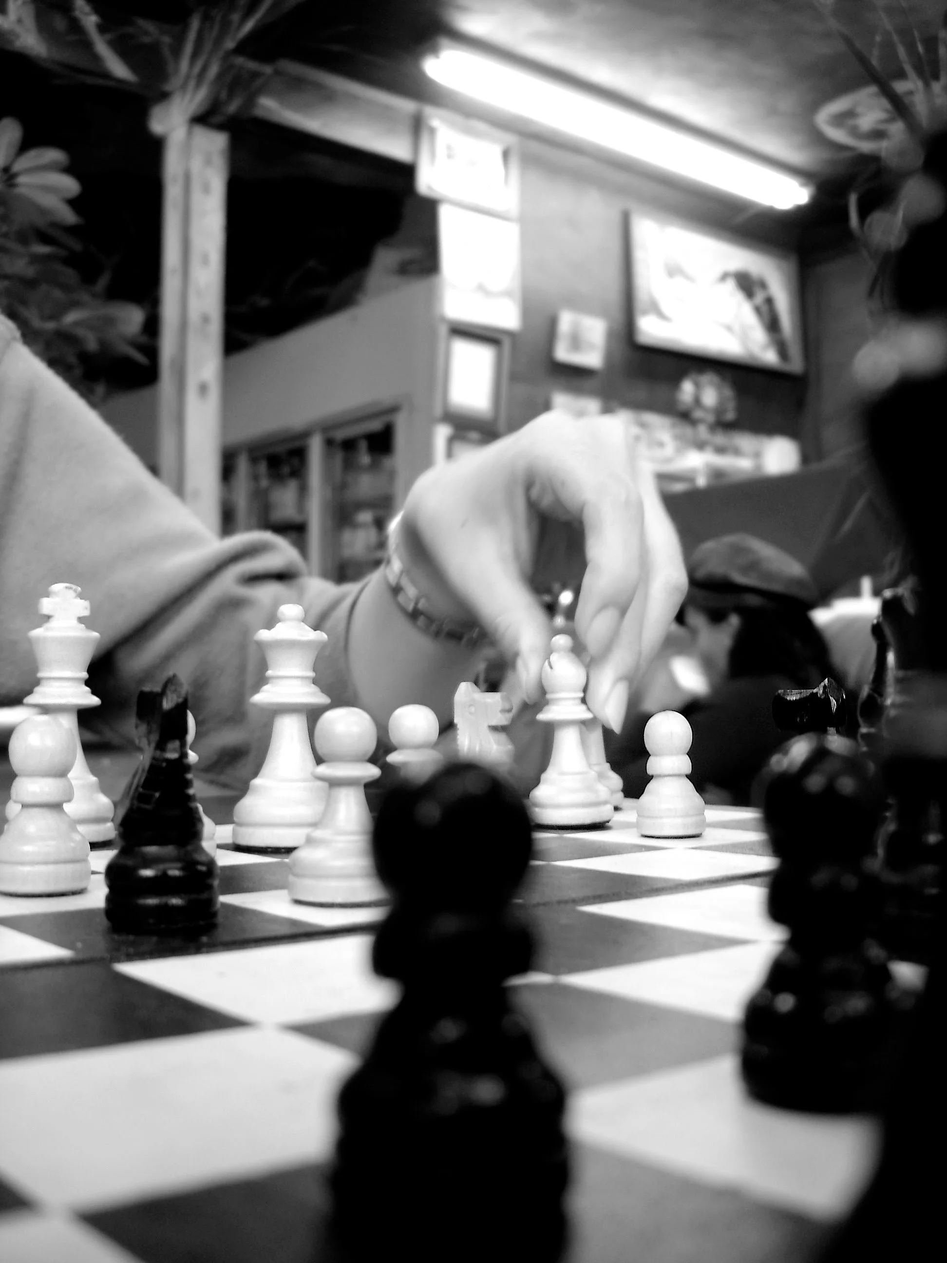 Close-up of a chess game with a person's hand moving a rook on the board in a cozy room with framed pictures on the wall.