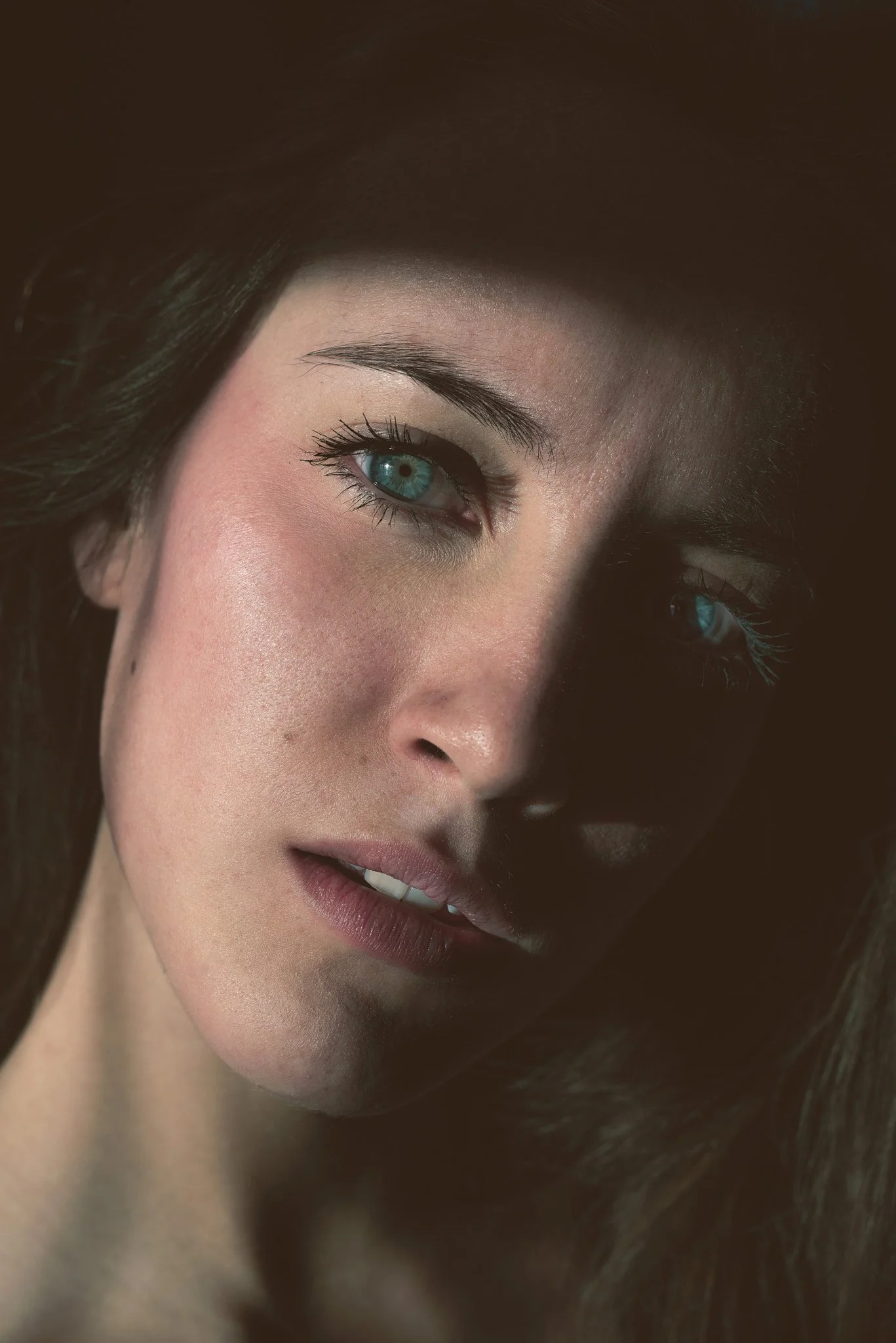 Close-up portrait of a woman with blue eyes, dark hair, and natural makeup, looking at the camera.