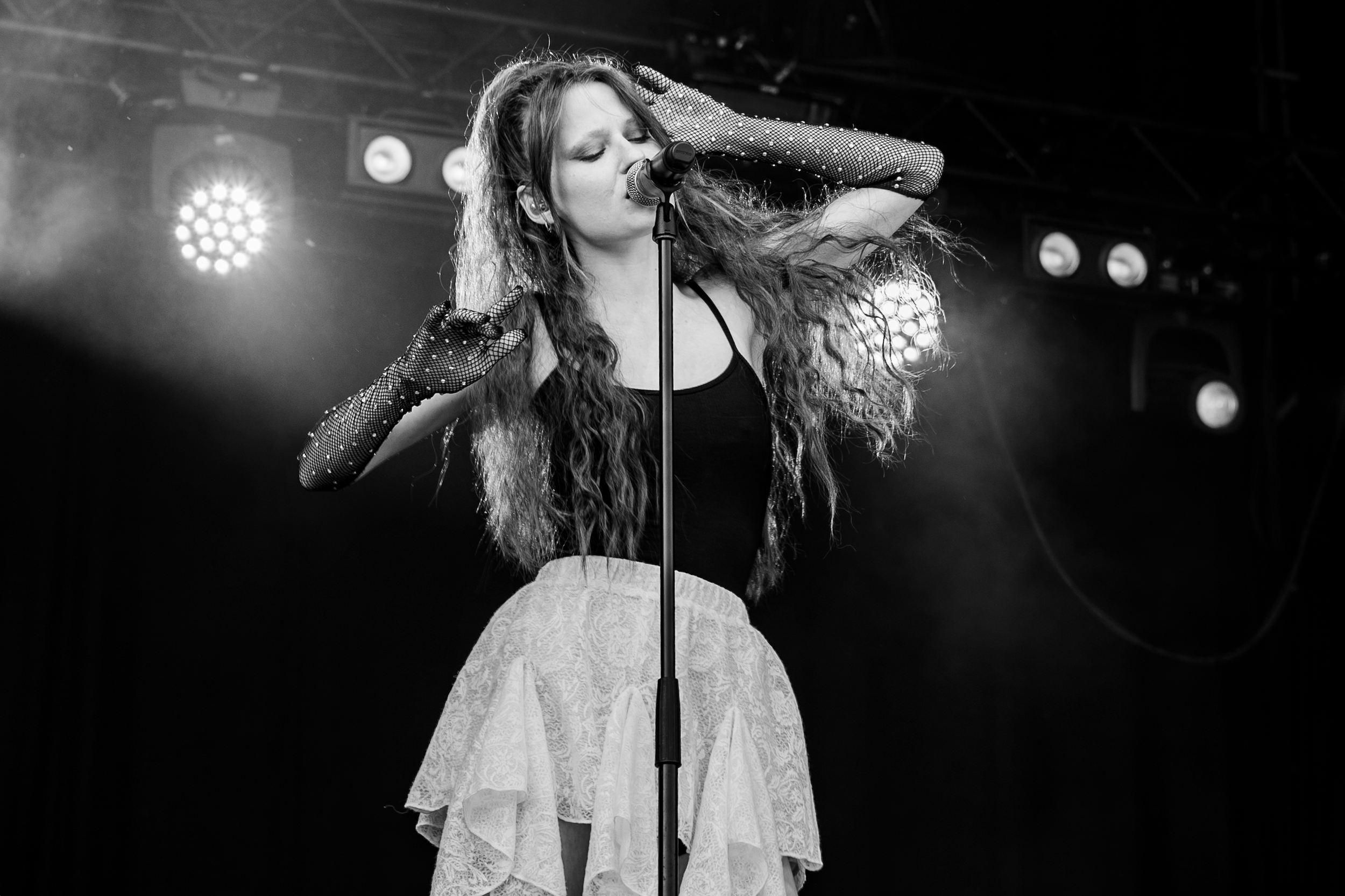 A woman singing into a microphone on stage, with stage lights in the background.