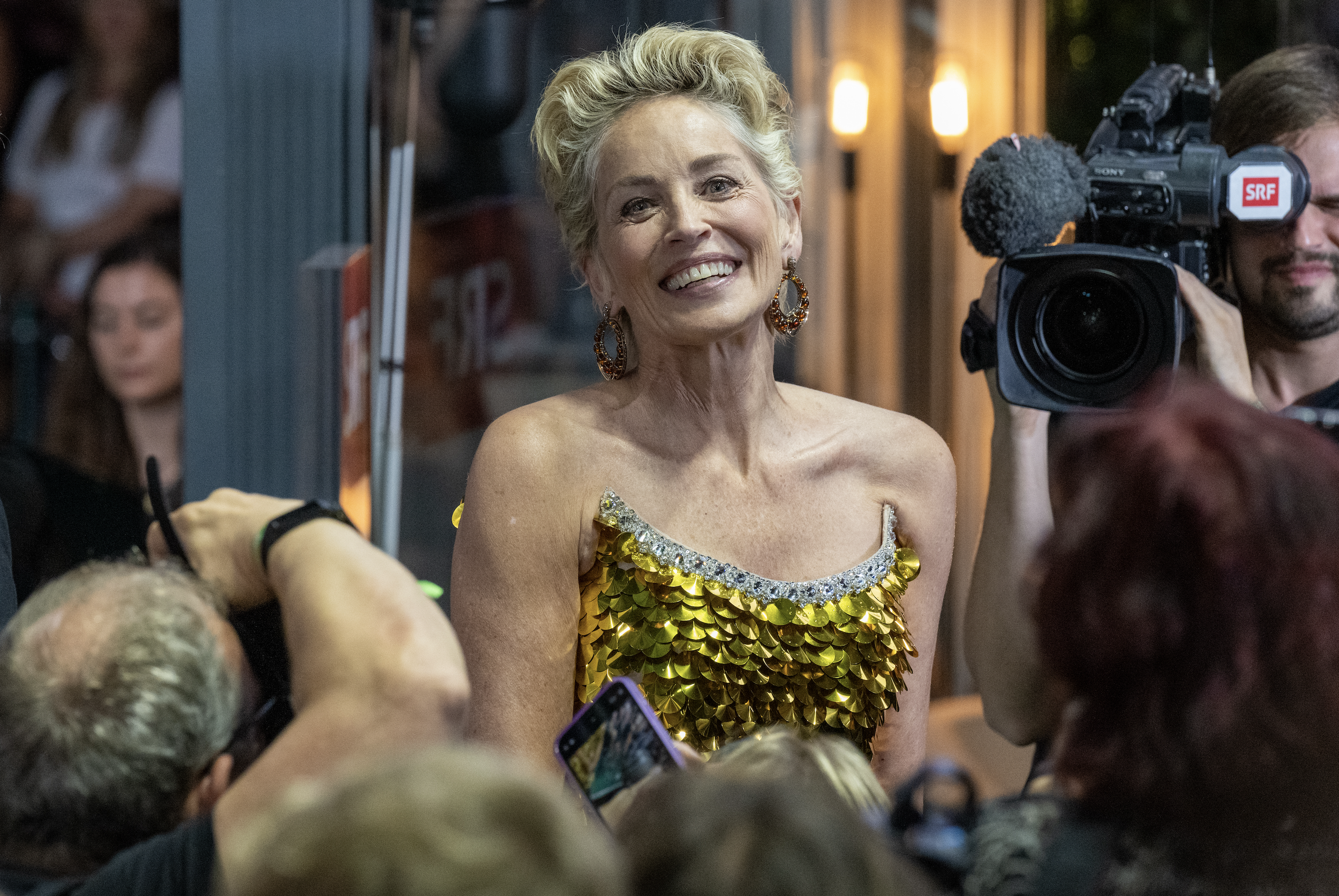 A woman wearing a gold, shiny, sequined dress being interviewed by photographers.