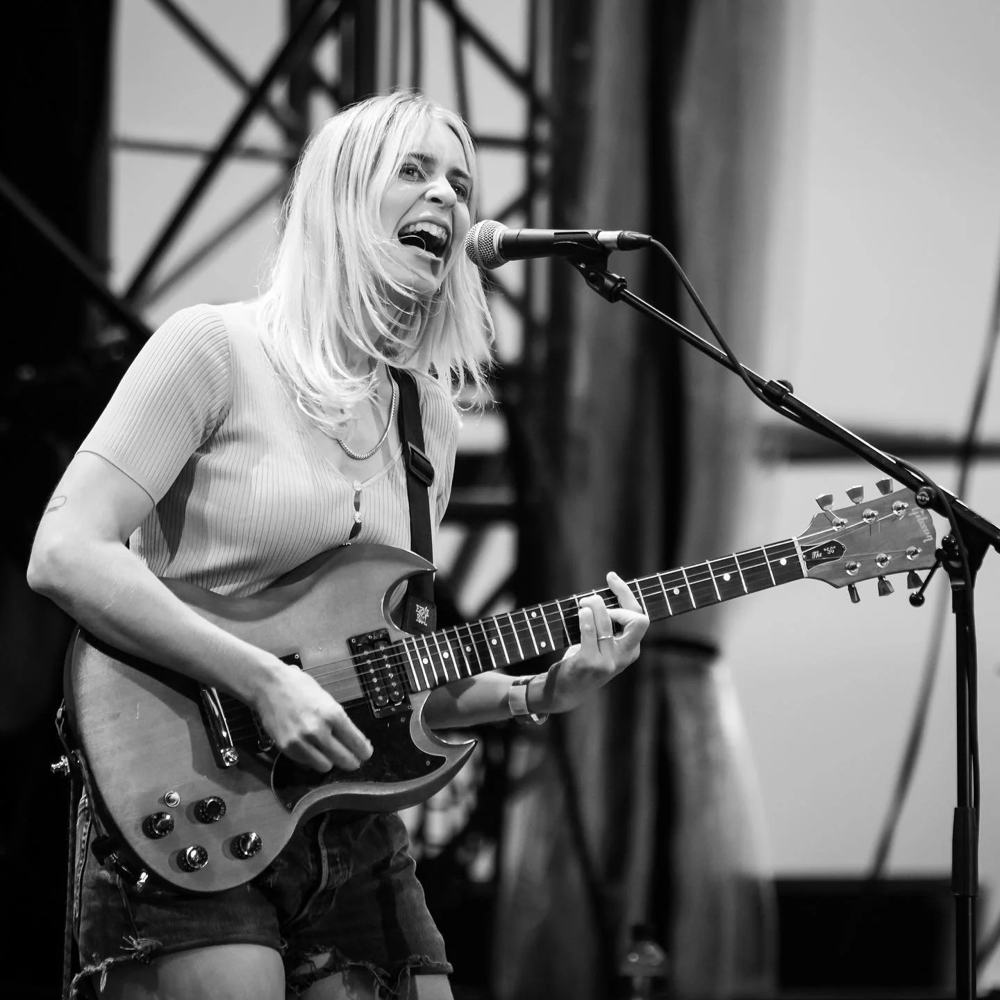 A woman with blonde hair singing and playing an electric guitar on stage, black and white photo.