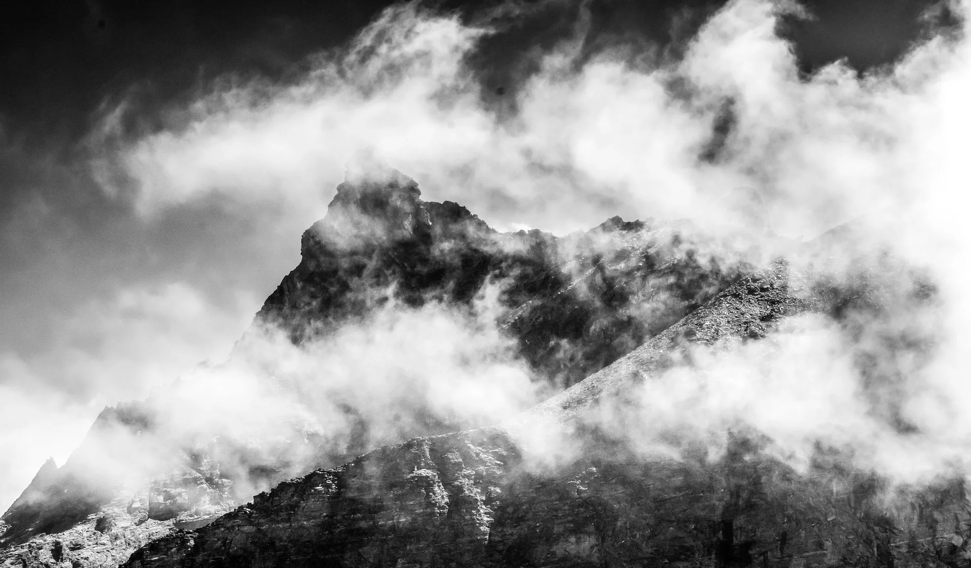 Black and white photo of a mountain peak shrouded in clouds and mist.