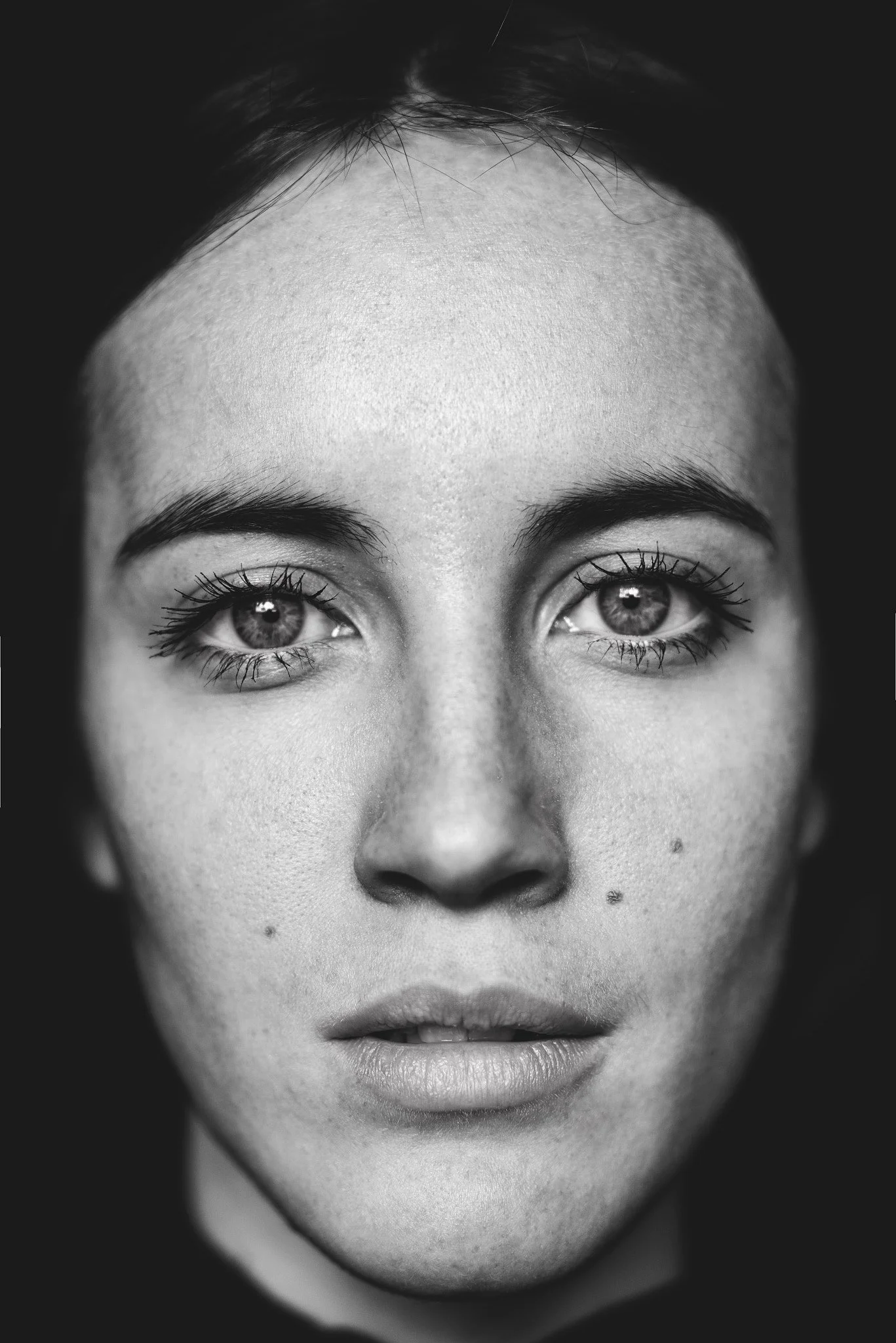 Close-up black and white portrait of a young woman's face, focusing on her eyes, eyebrows, nose, and lips.