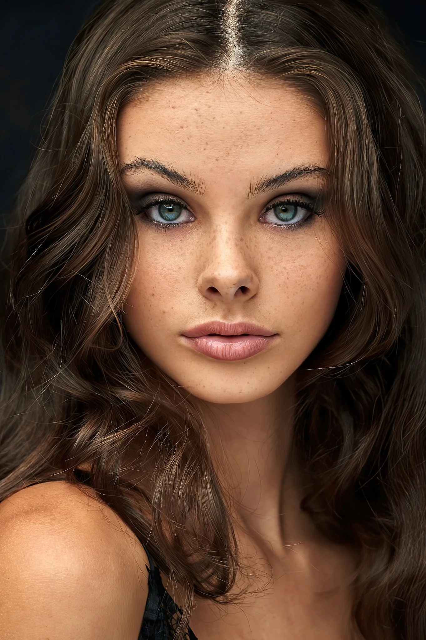 Close-up of a young woman with wavy brown hair, blue eyes, freckles, and a neutral expression.