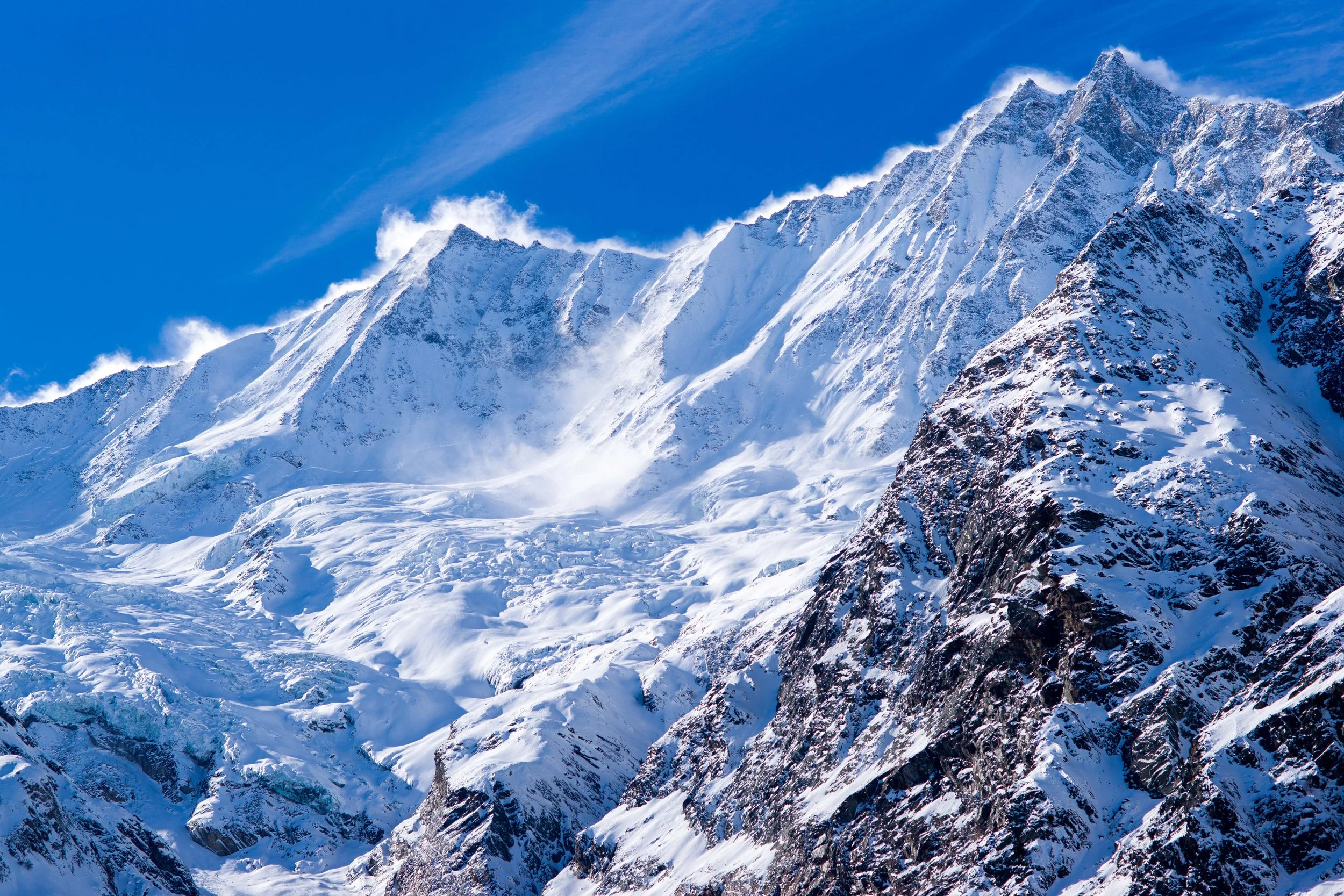 Snow-covered mountains under a blue sky with wispy clouds.