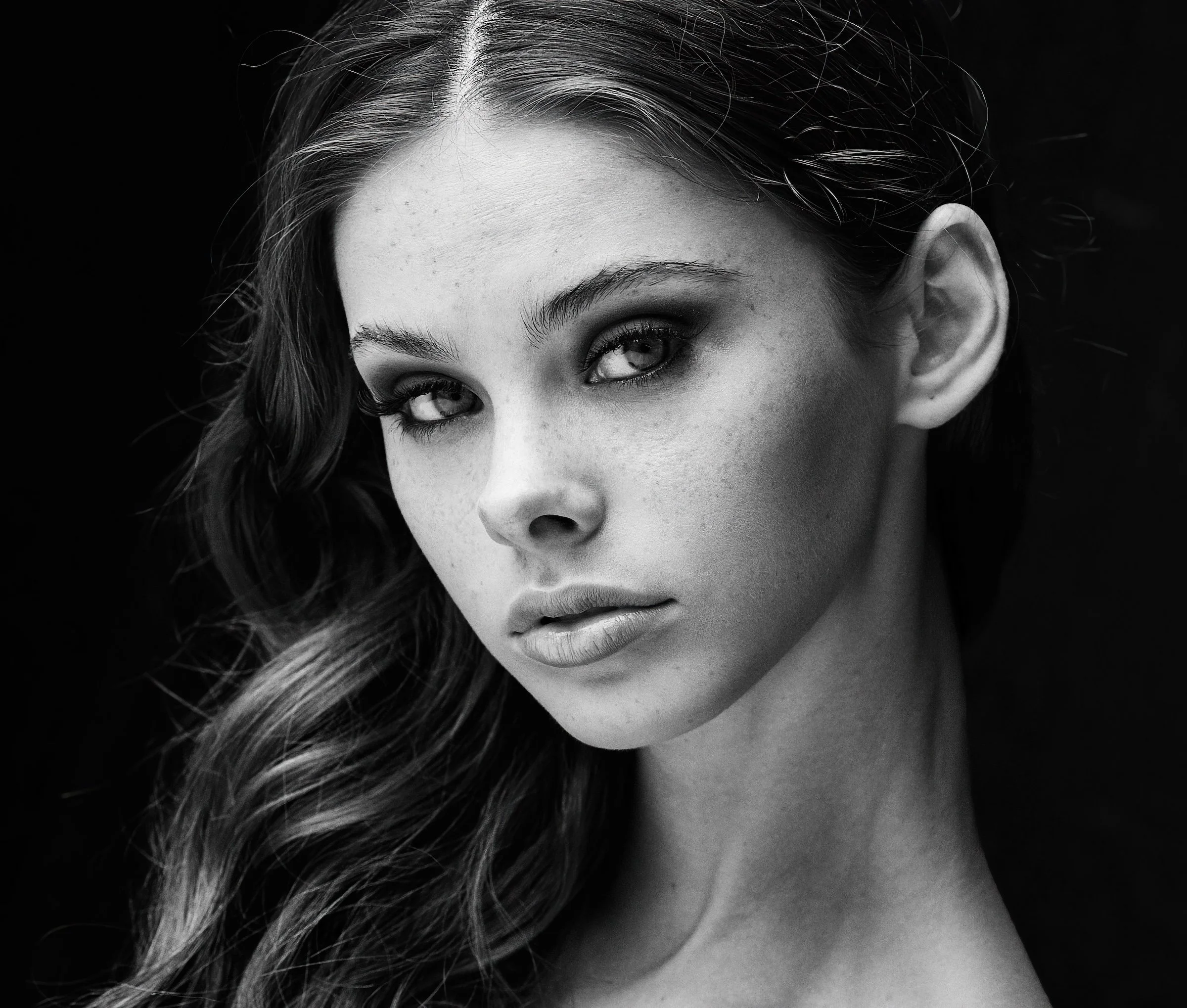 Black and white portrait of a woman with wavy hair, looking directly at the camera with a serious expression.