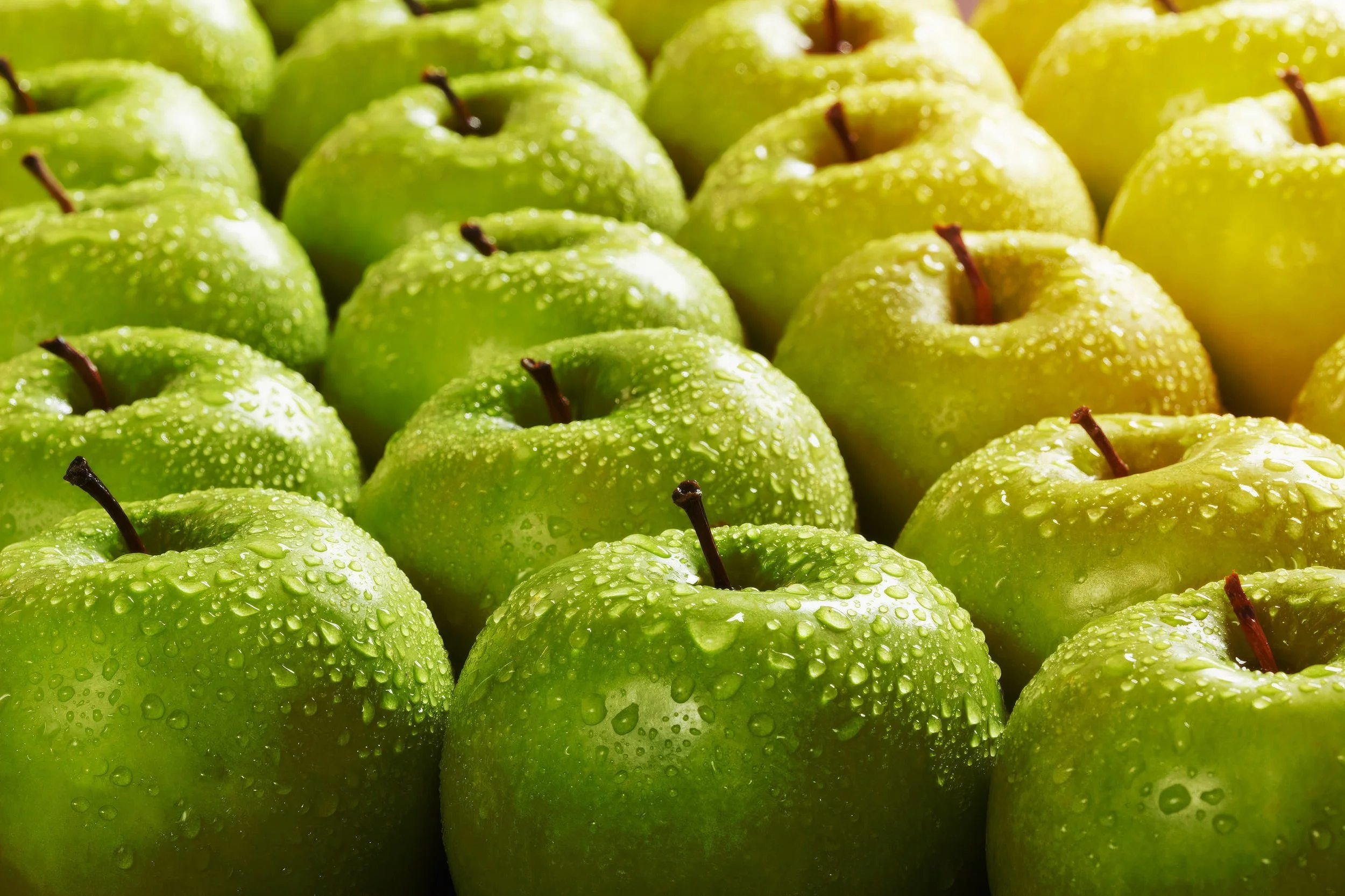Close-up of fresh green apples with water droplets on their surface.