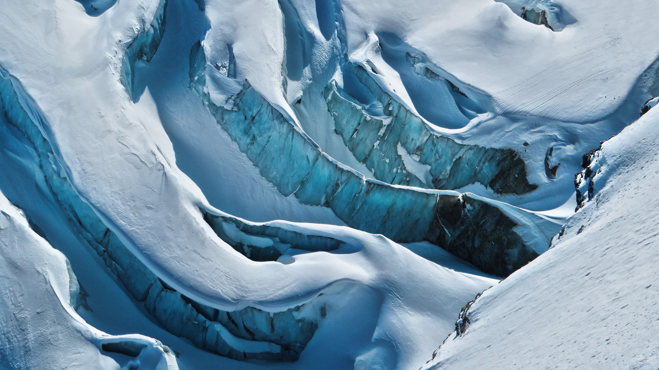 A glacier with blue ice crevasses and snow covering surrounding areas.