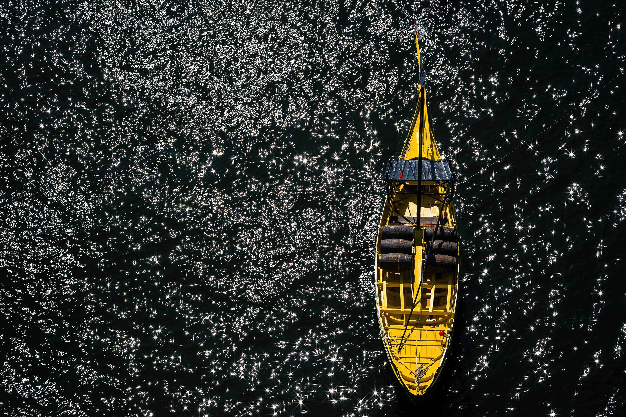 Overhead view of a yellow boat on dark water with sunlight reflecting off the surface.