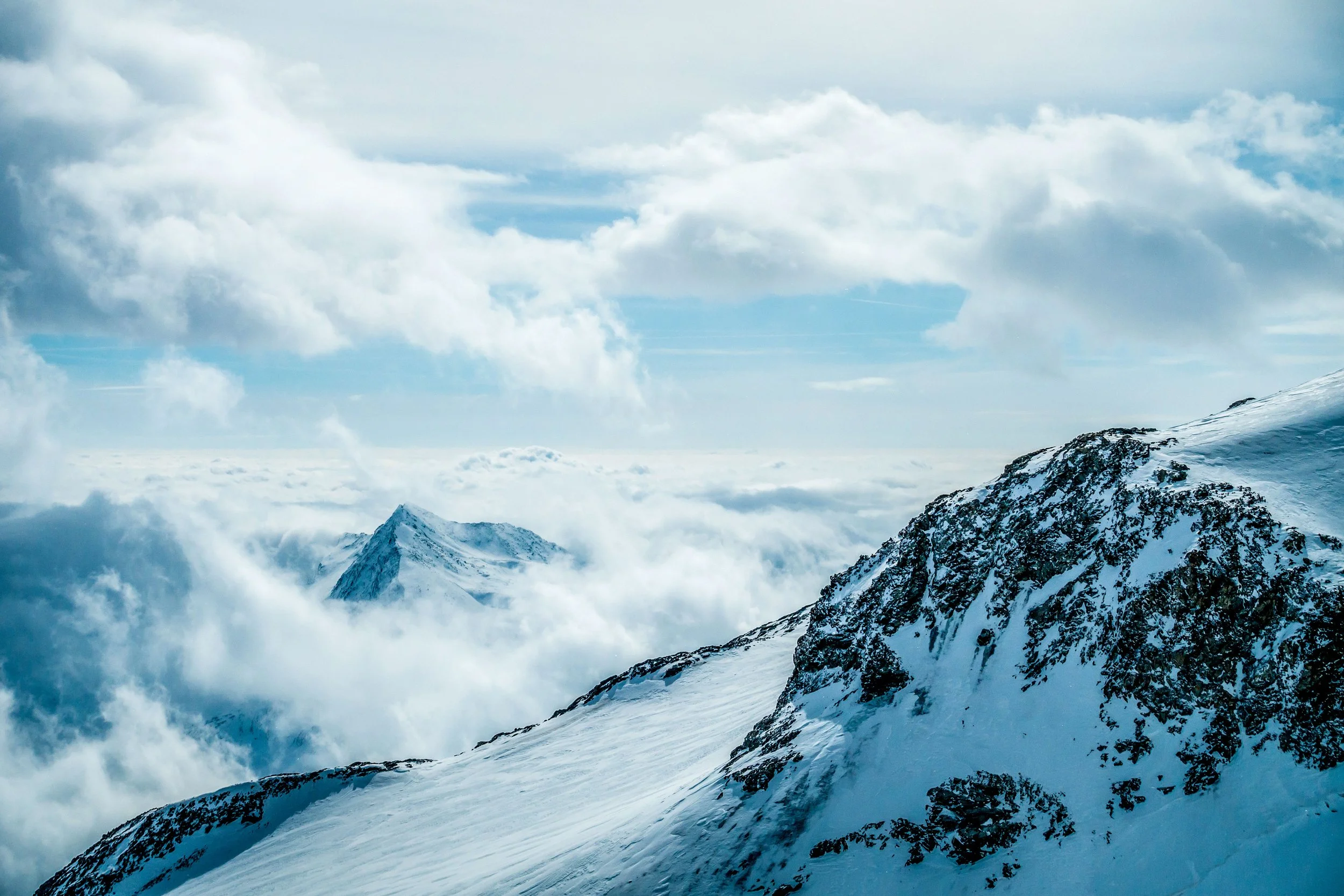Snow-covered mountain peaks with clouds and a blue sky.