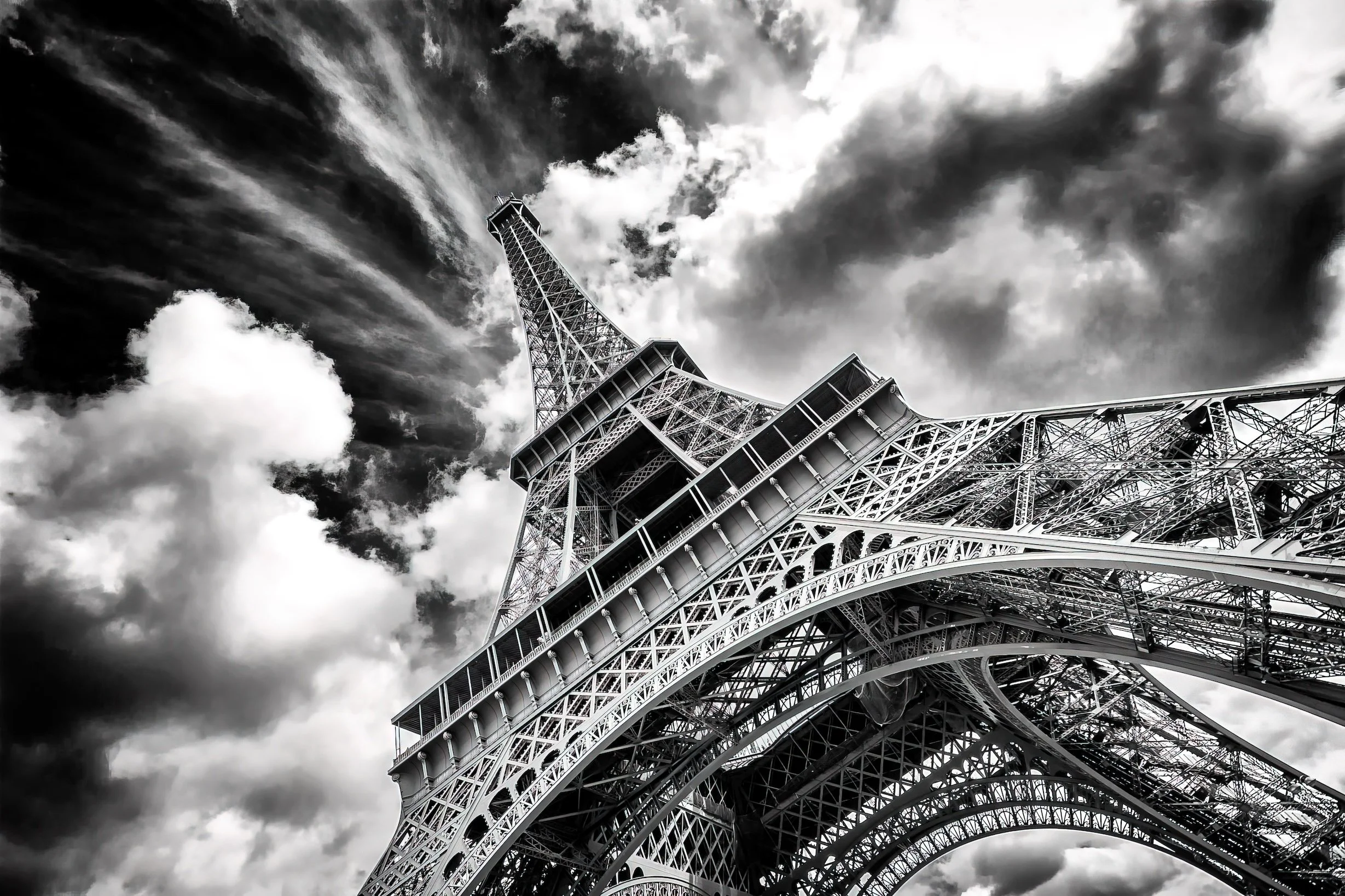 Low-angle black and white photo of the Eiffel Tower with dramatic clouds in the sky.