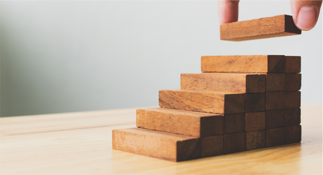 A hand stacking a wooden block on top of a pyramid of wooden blocks.