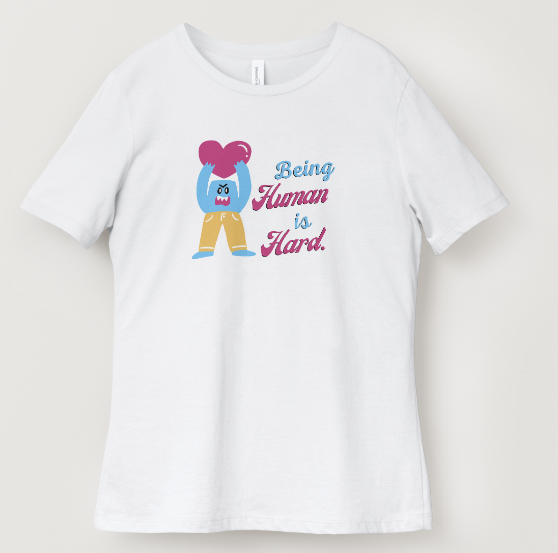 White T-shirt with a cartoon character holding a pink heart and the text 'Being Human is Hard.'