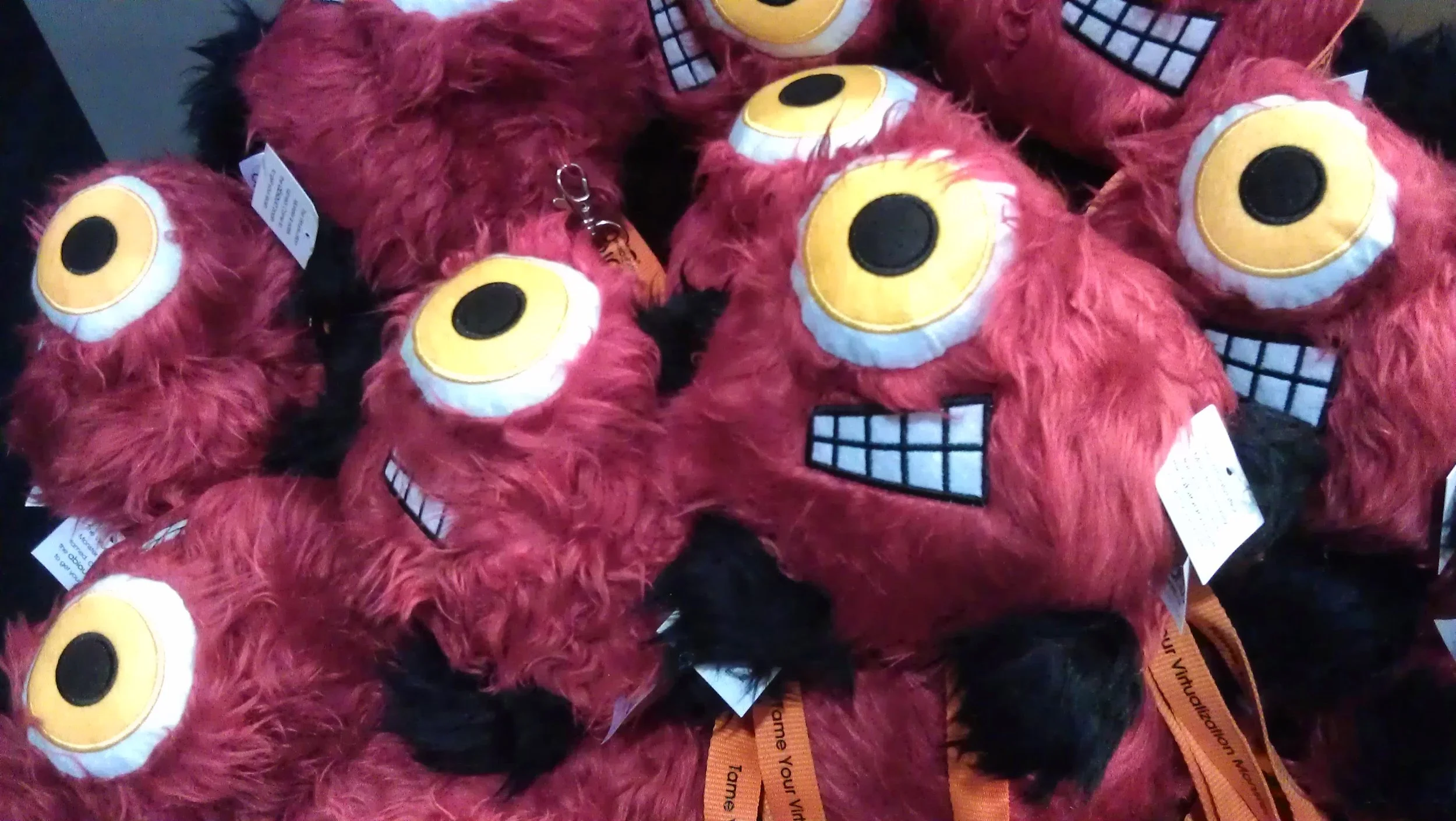 A pile of red furry plush toys with large cartoonish yellow eyes, big grins showing teeth, and black fur accents.