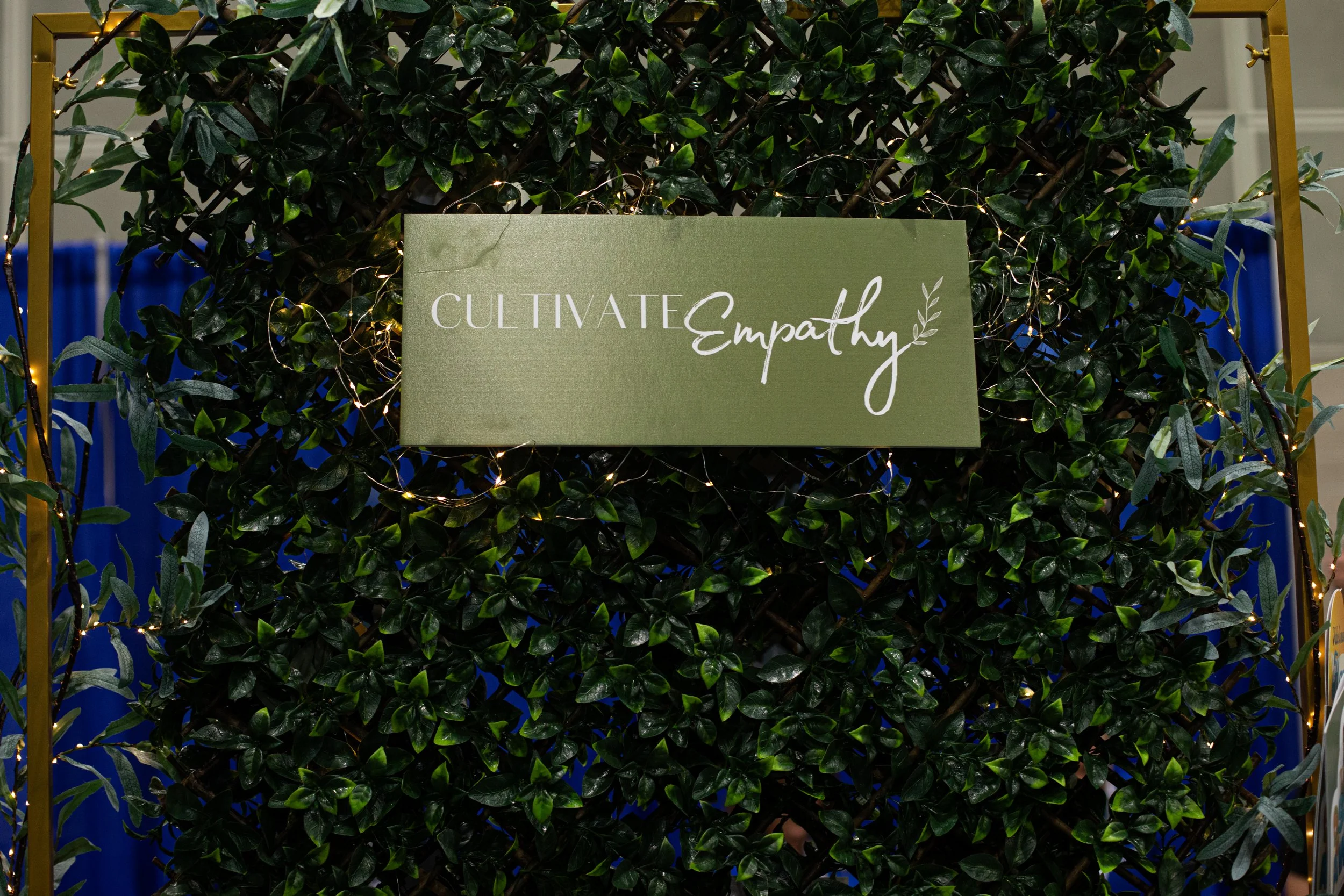 A decorative display with a lush green bush and a sign that reads 'Cultivate Empathy,' surrounded by small string lights.
