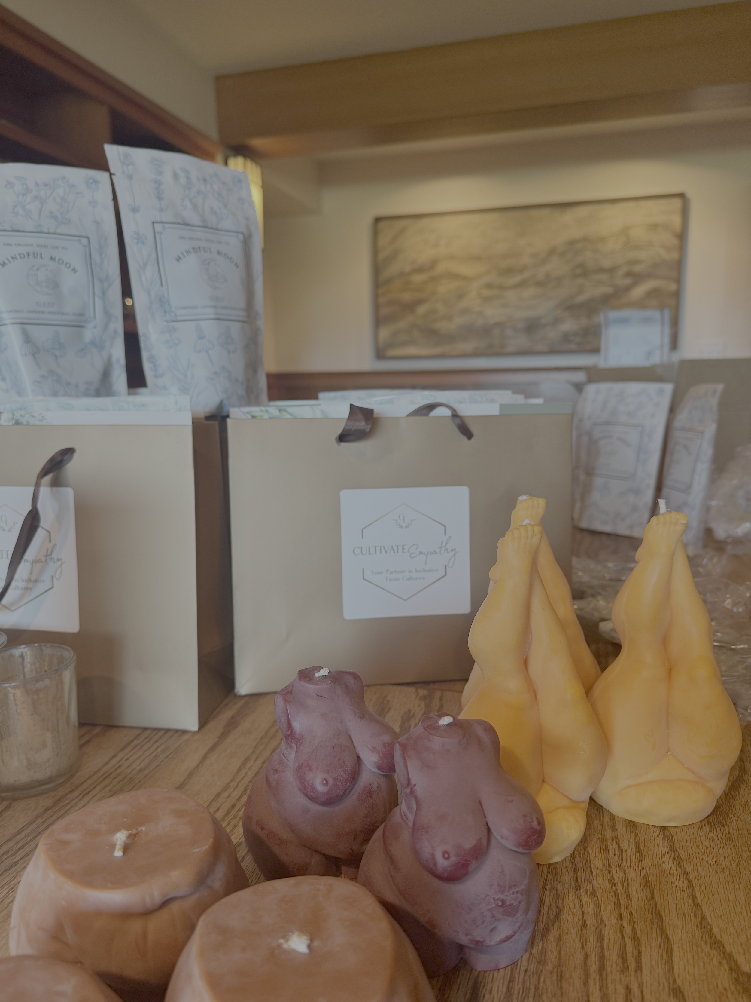 Decorative candles on a wooden table with gift bags and a painting in the background.