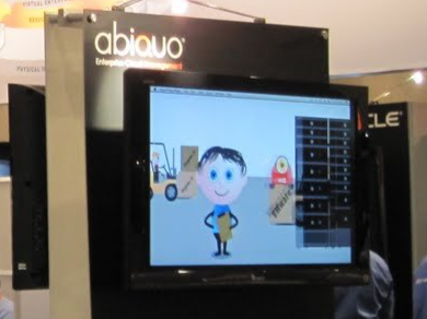 A monitor displaying a cartoon character with a yellow shirt in front of a black box labeled Abiau, in an exhibition or store setting.