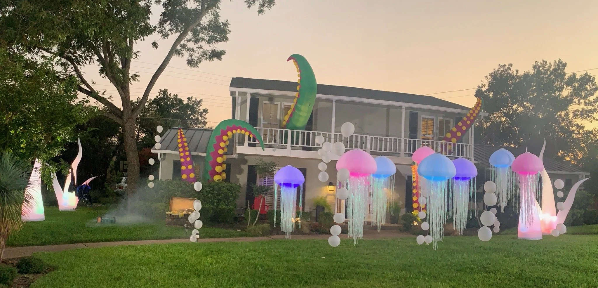 Decorative outdoor scene with colorful mushroom-shaped lanterns and abstract tentacle sculptures, set against a house with a balcony at dusk.