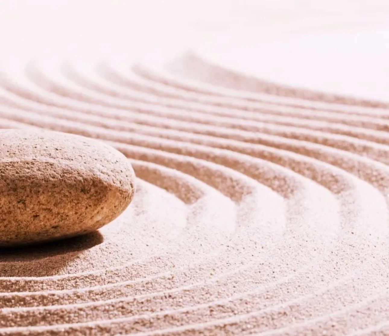 A smooth stone on a sandy surface with engraved ripple patterns in the sand.